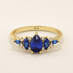 14k gold anniversary ring featuring five pear-cut sapphire gemstones. Elegant and symmetrical gemstone band design.