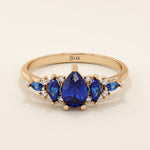 14k gold anniversary ring featuring five pear-cut sapphire gemstones. Elegant and symmetrical gemstone band design.