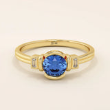 14k gold ring featuring a half bezel round sapphire with baguette moissanite accents. A modern gemstone anniversary band with elegant sparkle.