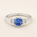 14k gold ring featuring a half bezel round sapphire with baguette moissanite accents. A modern gemstone anniversary band with elegant sparkle.