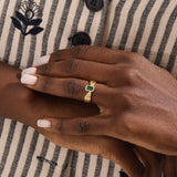 A model wears a vintage-inspired 14k gold statement ring with a bezel-set emerald cut green gemstone. The bold rectangular ring sits comfortably on the finger, catching the light with its glossy finish.