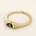 Angled view of a 14k yellow gold ring showcasing a vivid oval green gemstone in a ribbed split mount.