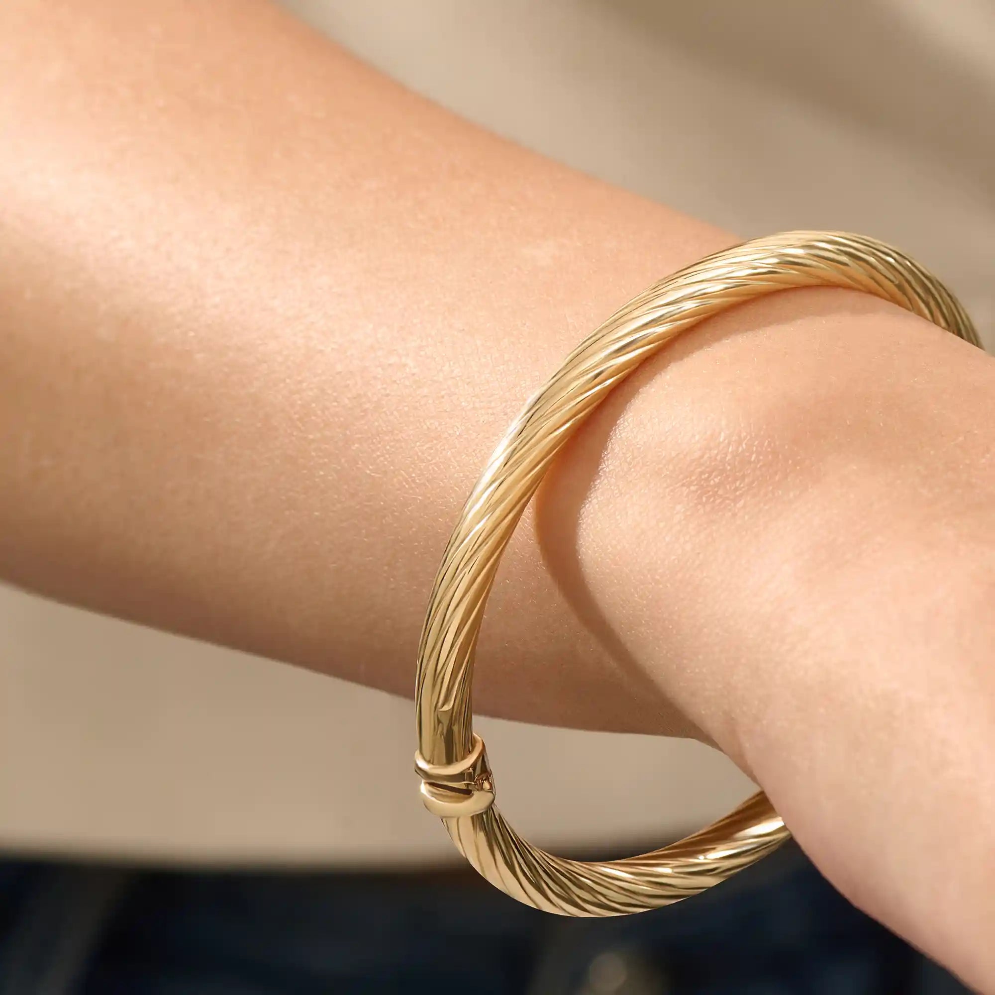 Close-up of a model’s arm wearing a 14k yellow gold rope bangle bracelet with a twisted rope design and polished shine.