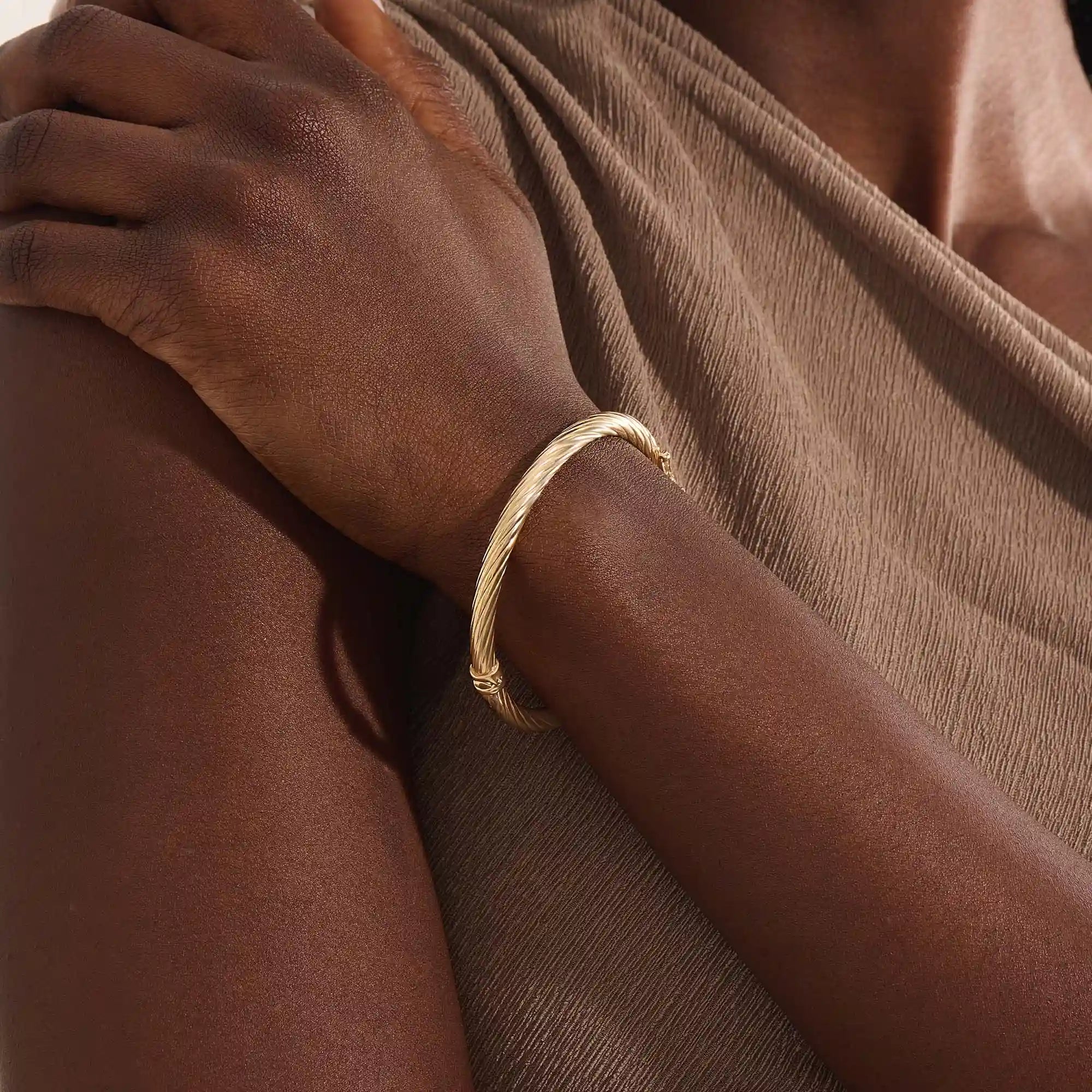 Close-up of a model’s arm wearing a 14k yellow gold rope bangle bracelet with a twisted rope design and polished shine.
