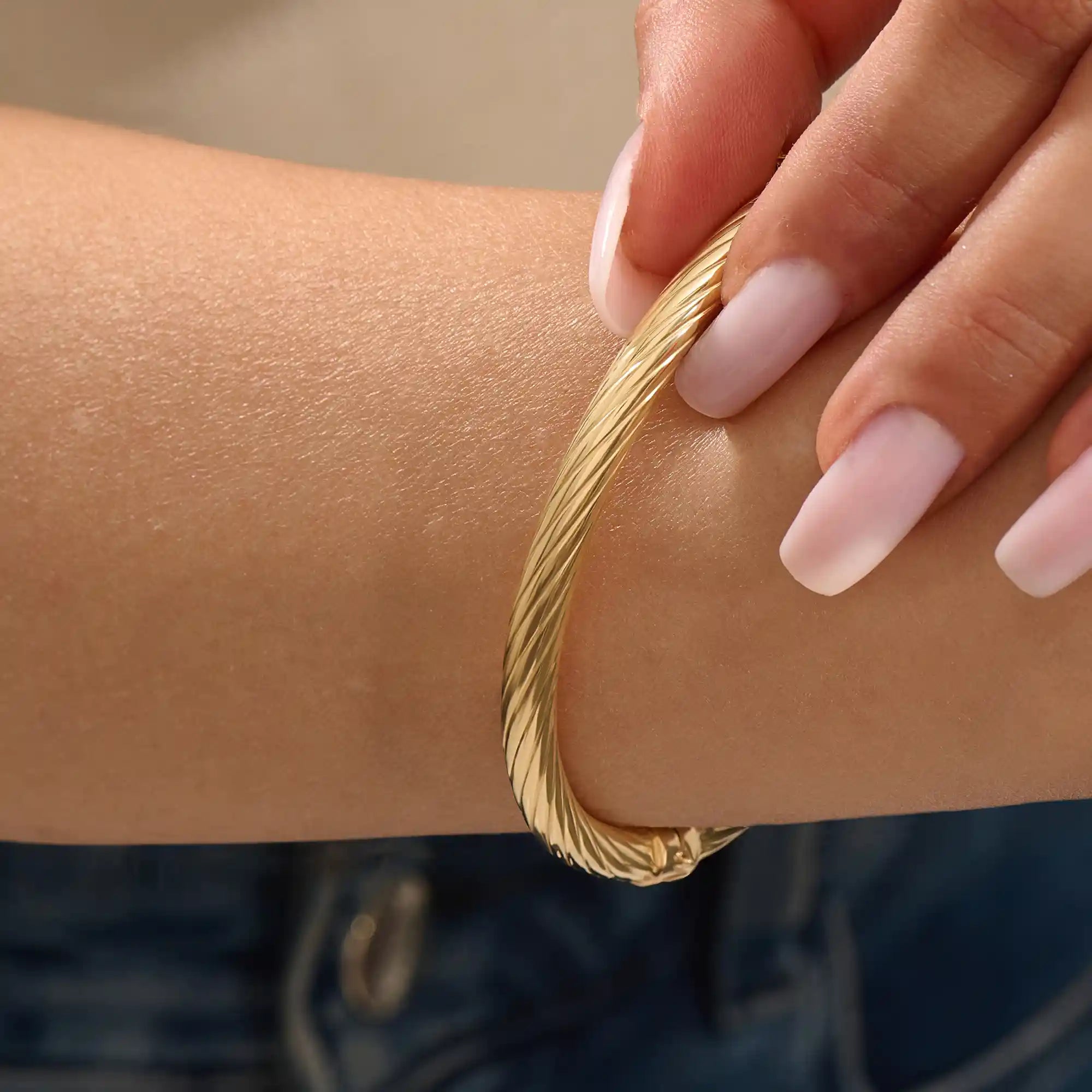 Close-up of a model’s arm wearing a 14k yellow gold rope bangle bracelet with a twisted rope design and polished shine.