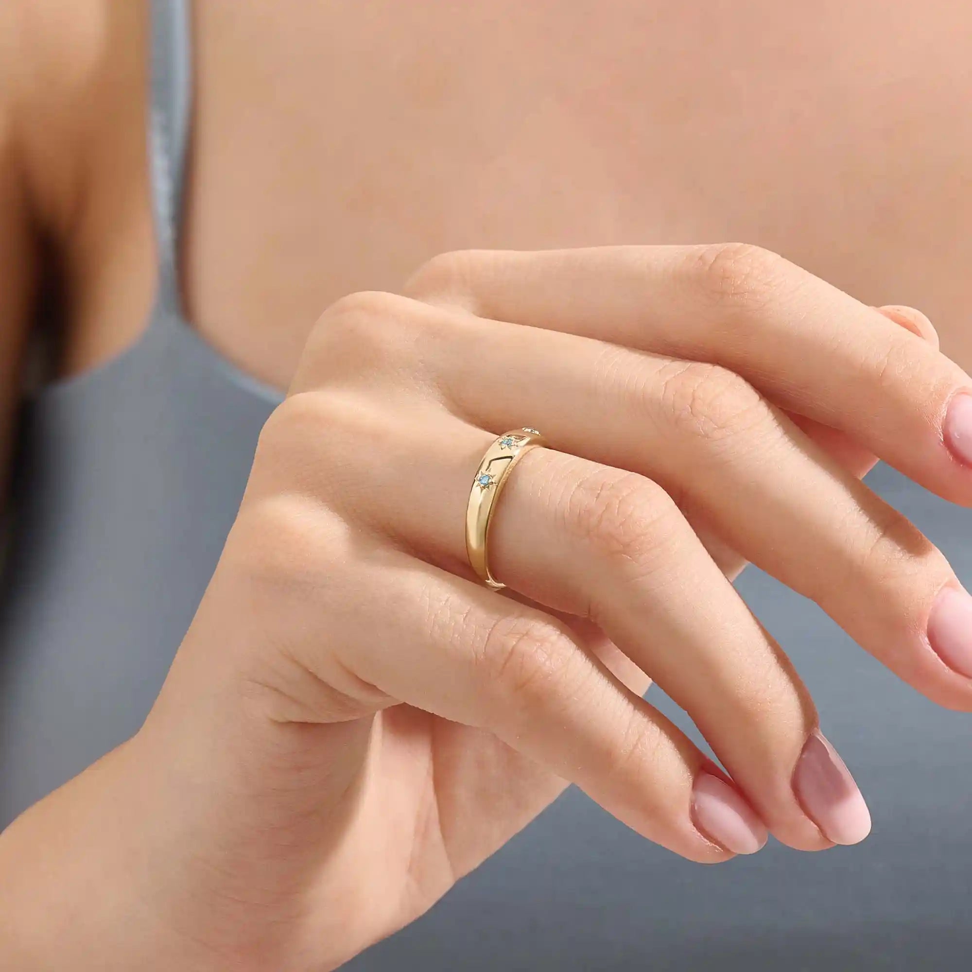Close-up of a model’s hand wearing a 14k yellow gold dome ring with aquamarine gemstones in starburst settings across the band.