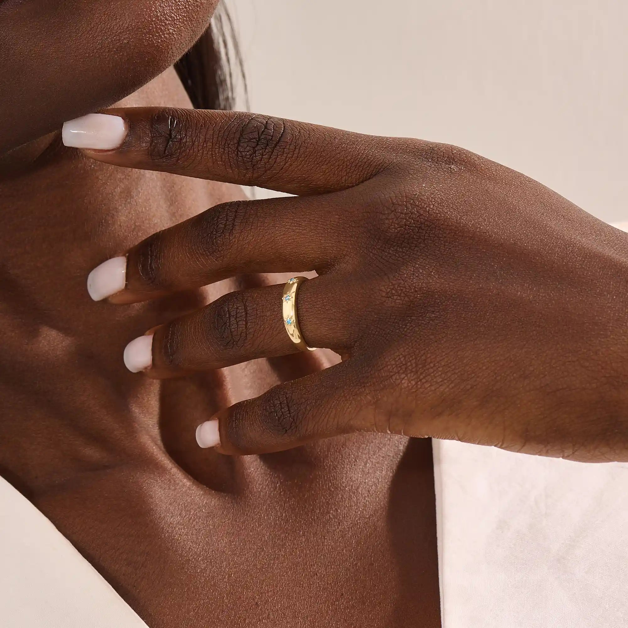 Close-up of a model’s hand wearing a 14k yellow gold dome ring with aquamarine gemstones in starburst settings across the band.