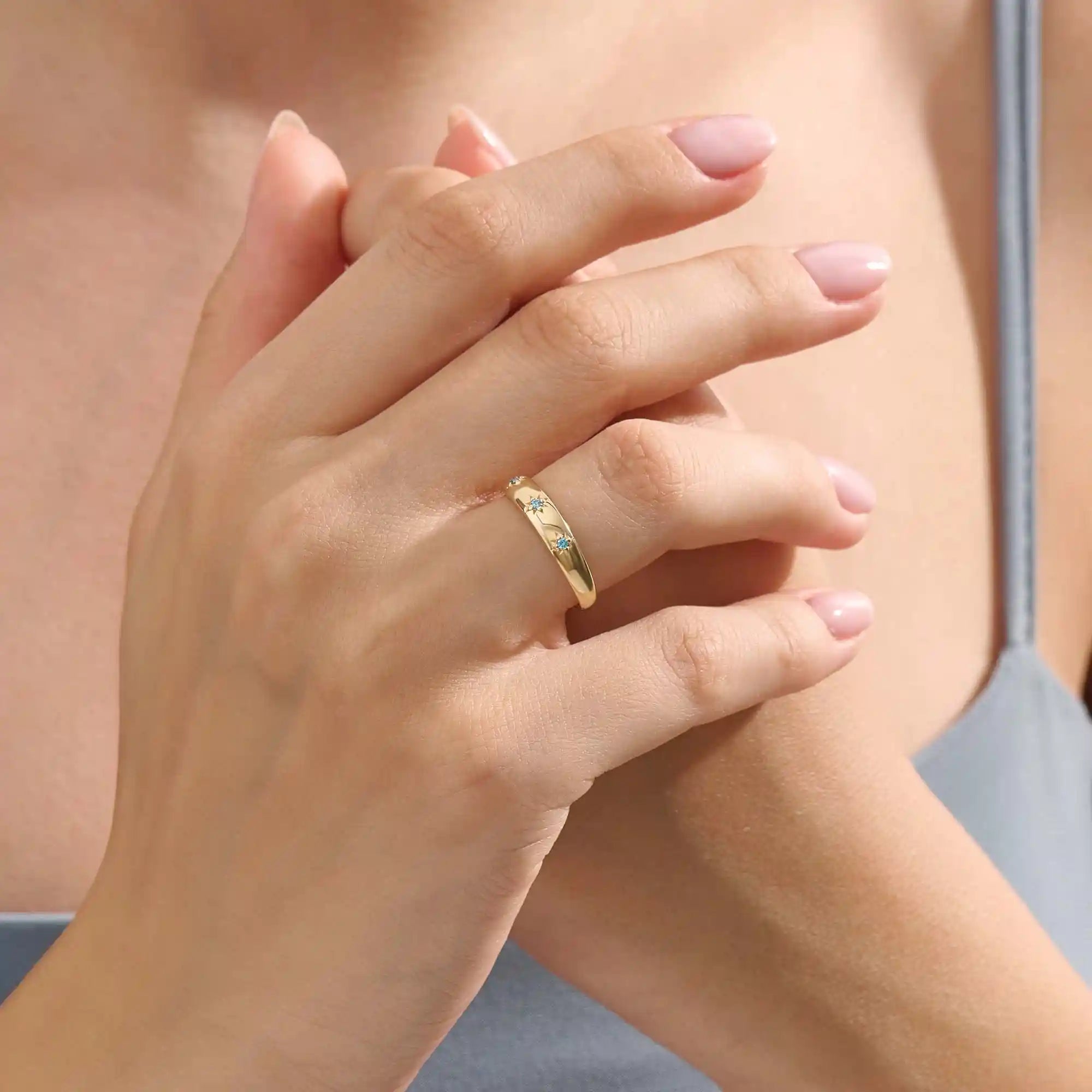 Close-up of a model’s hand wearing a 14k yellow gold dome ring with aquamarine gemstones in starburst settings across the band.