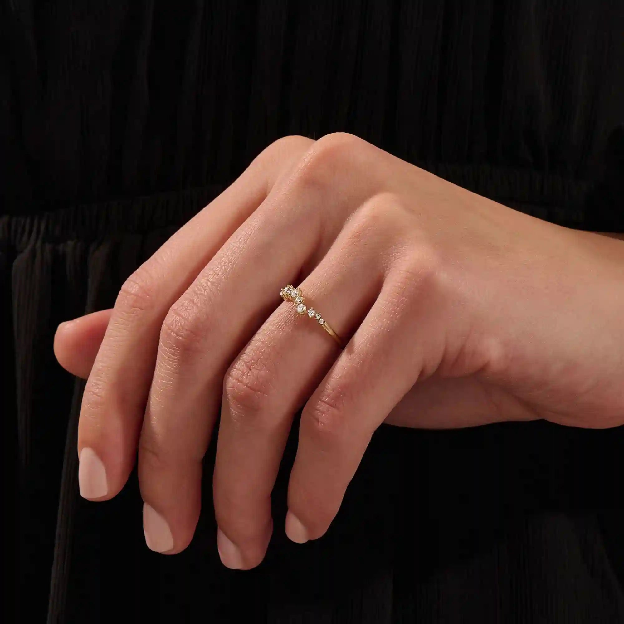 Close-up of a model’s hand wearing a 14k yellow gold pavé ring with alternating moissanite stone sizes.