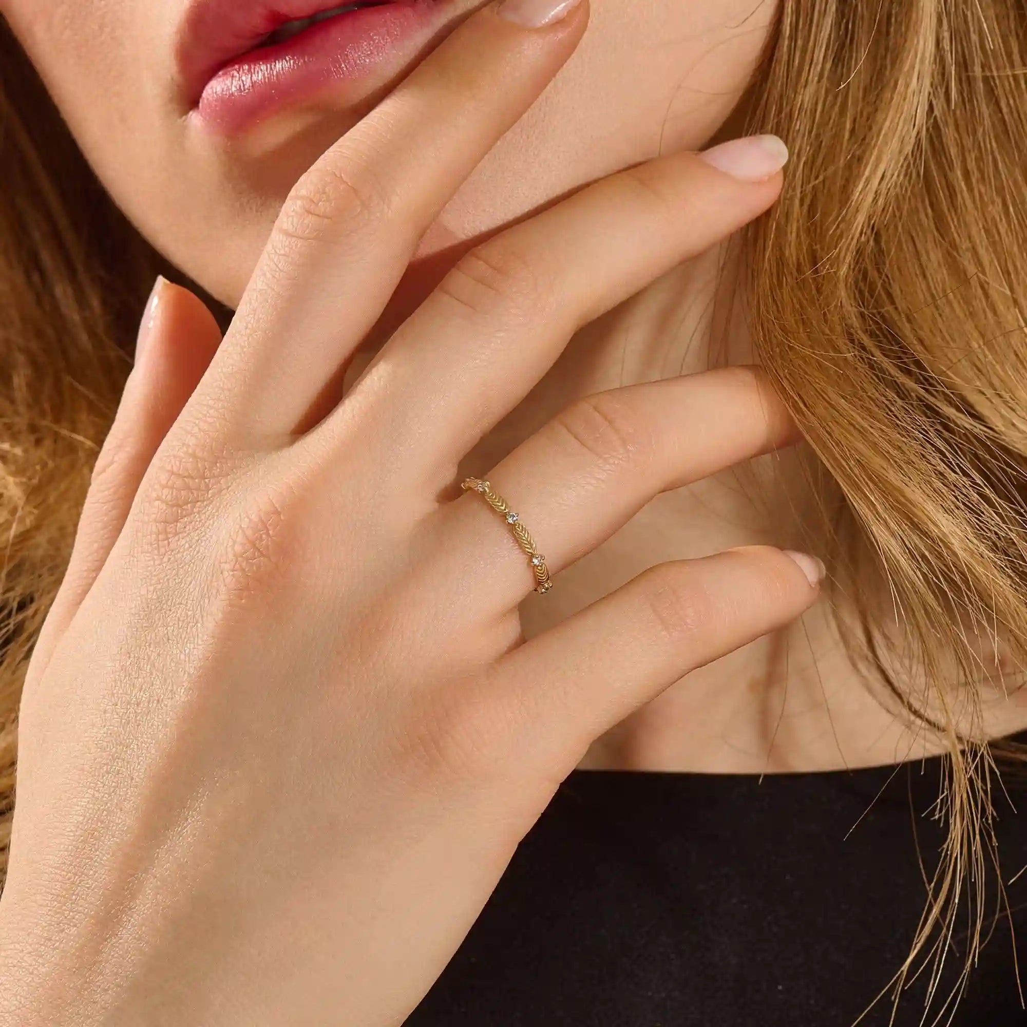 Close-up of a model’s hand wearing a 14k yellow gold ring with moissanite stones and engraved leaf motifs.