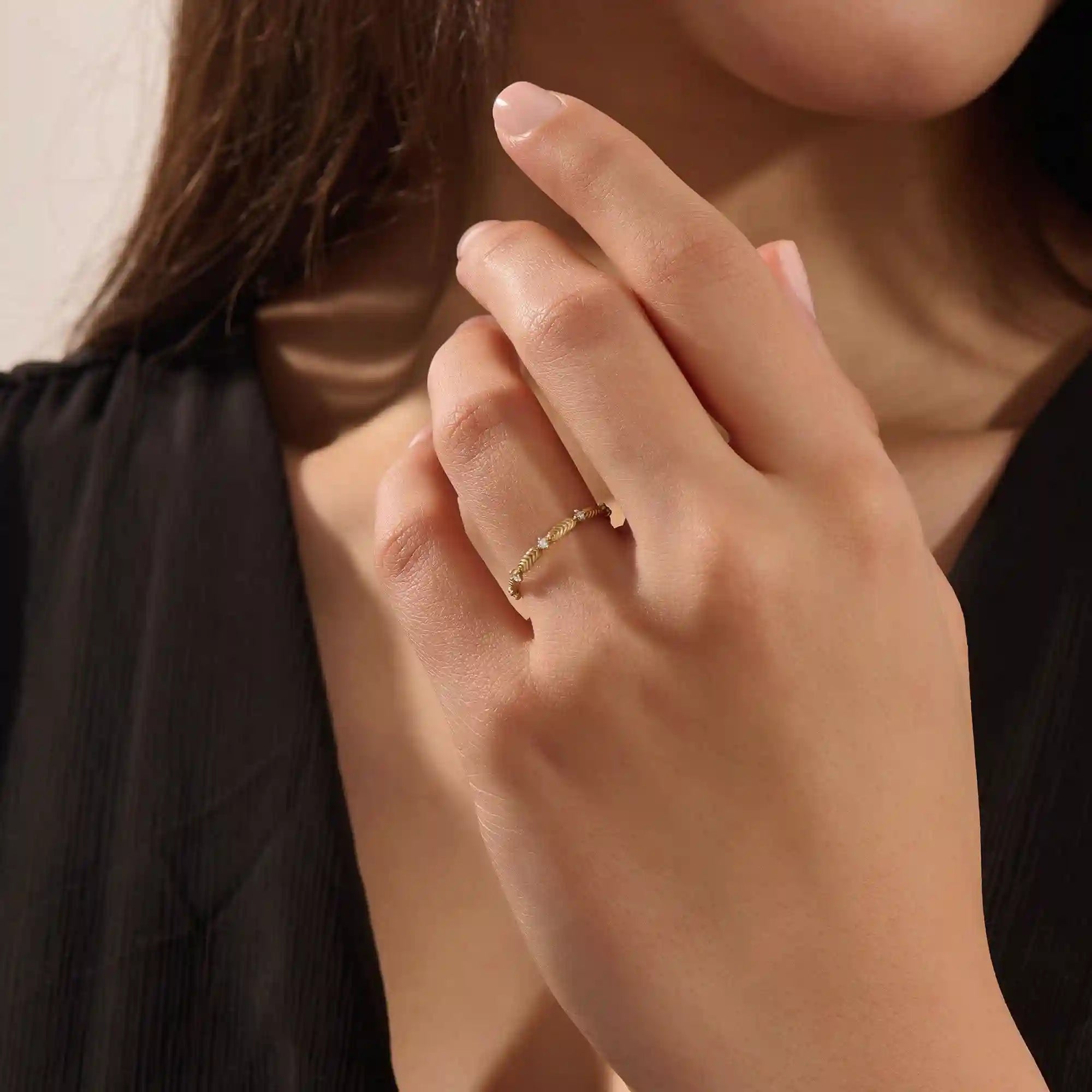Close-up of a model’s hand wearing a 14k yellow gold ring with moissanite stones and engraved leaf motifs.