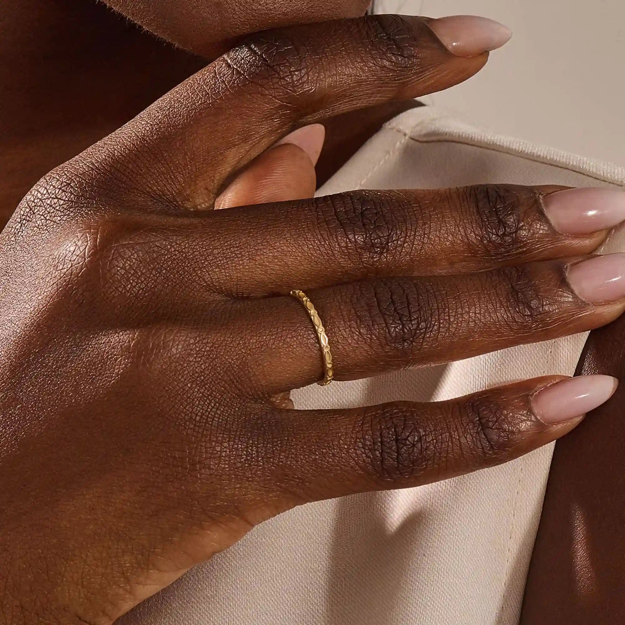 Close-up of a model’s hand wearing a 14k yellow gold slim wedding ring with a marquise-style engraved design.