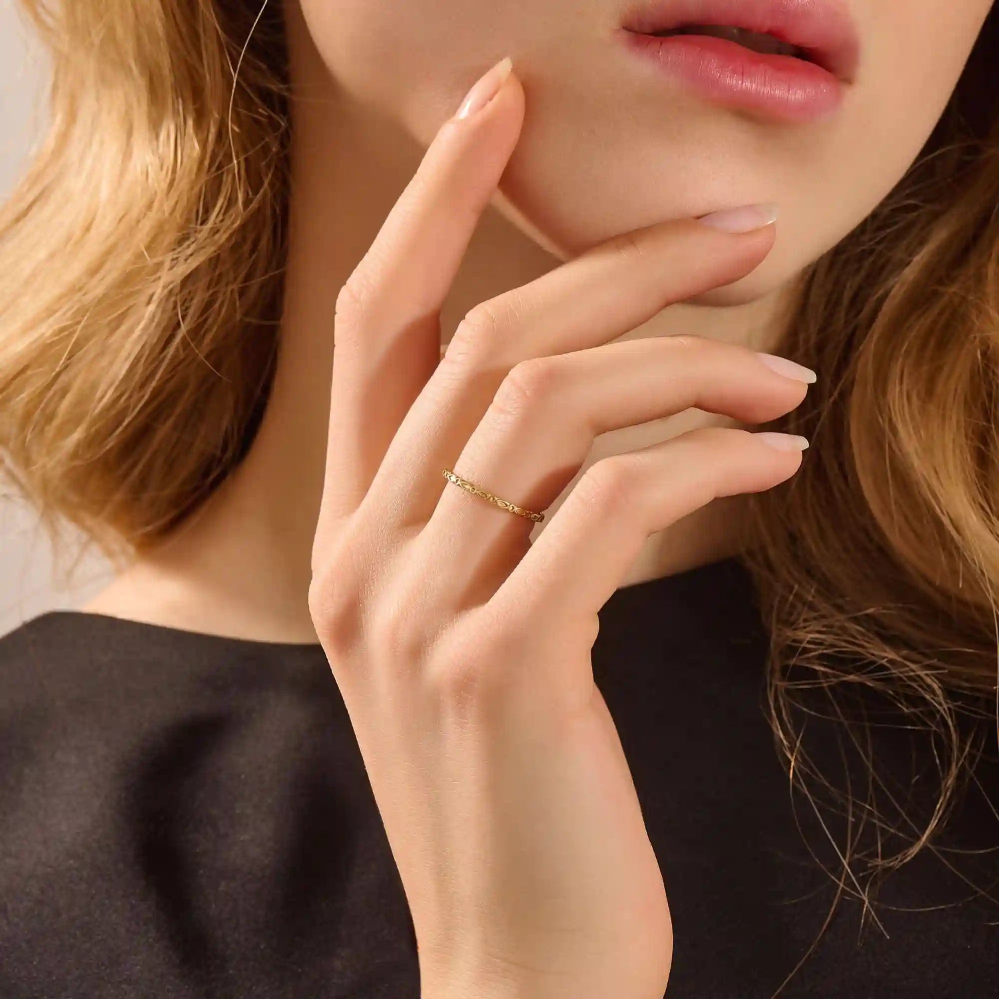Close-up of a model’s hand wearing a 14k yellow gold slim wedding ring with a marquise-style engraved design.