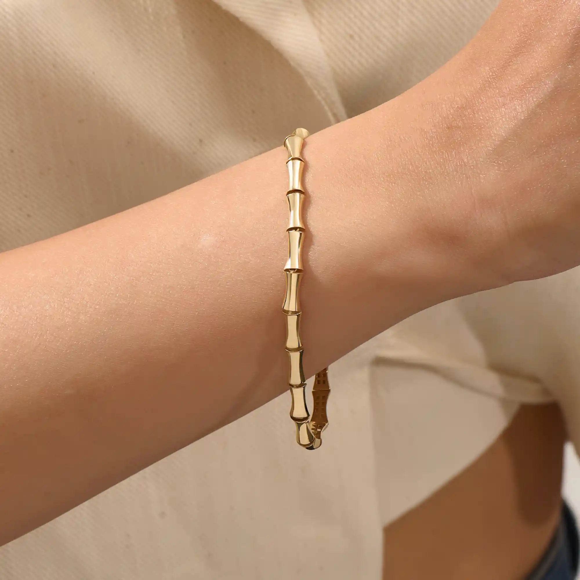 Close-up of a model’s wrist wearing a 14k yellow gold bone bracelet with bold curved links in a polished statement design.