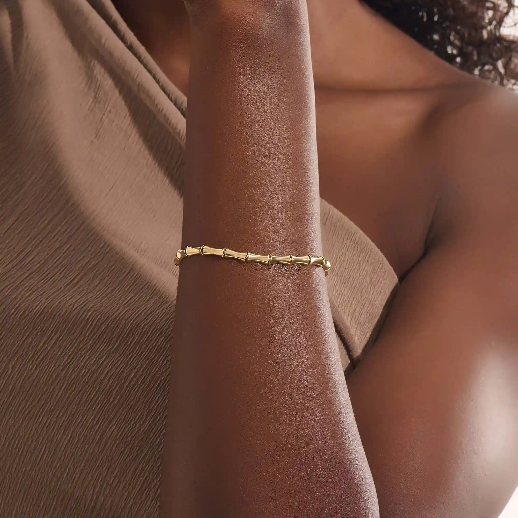 Close-up of a model’s wrist wearing a 14k yellow gold bone bracelet with bold curved links in a polished statement design.
