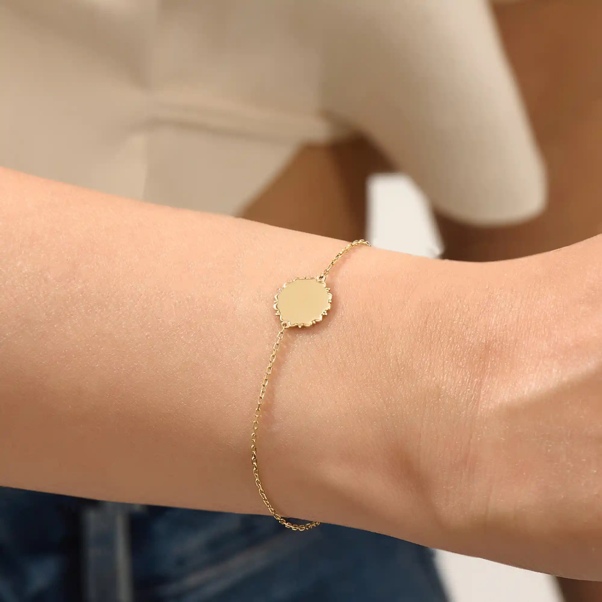 Close-up of a model’s wrist wearing a 14k yellow gold sun bracelet with a round medallion and delicate chain design.