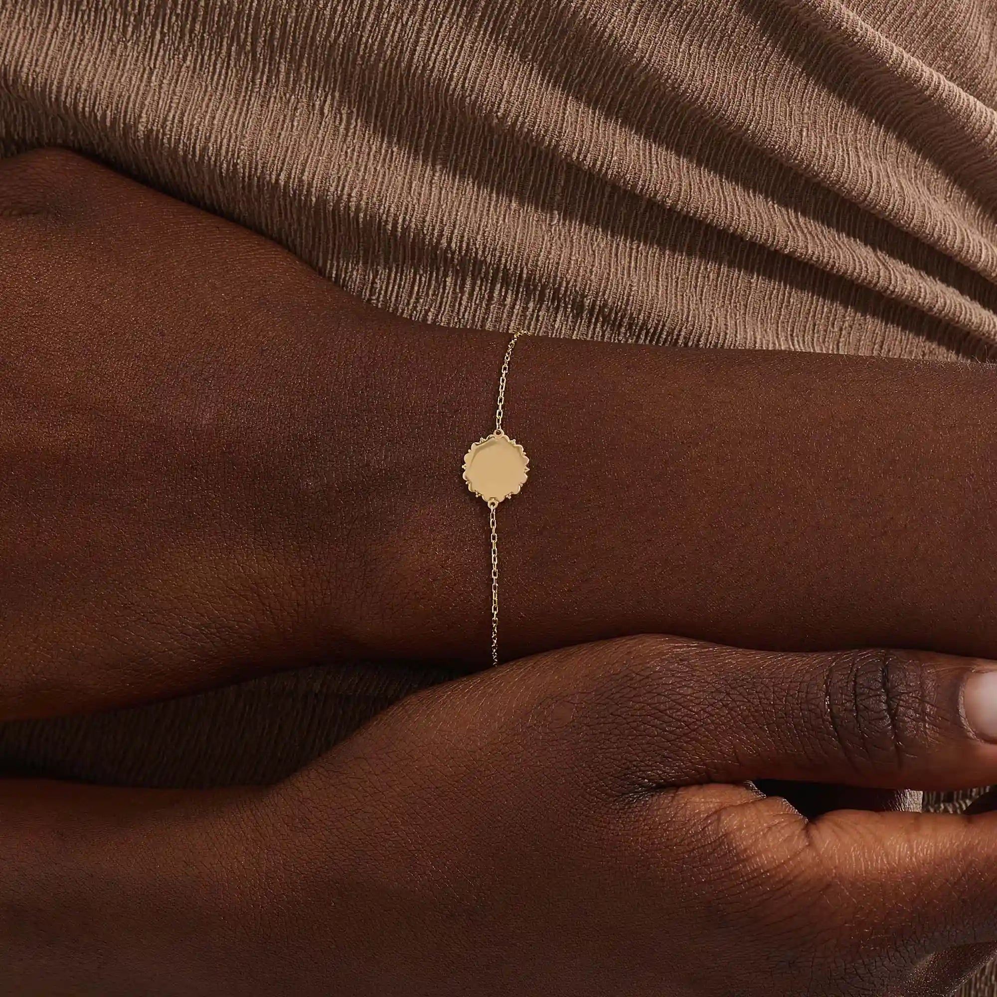 Close-up of a model’s wrist wearing a 14k yellow gold sun bracelet with a round medallion and delicate chain design.