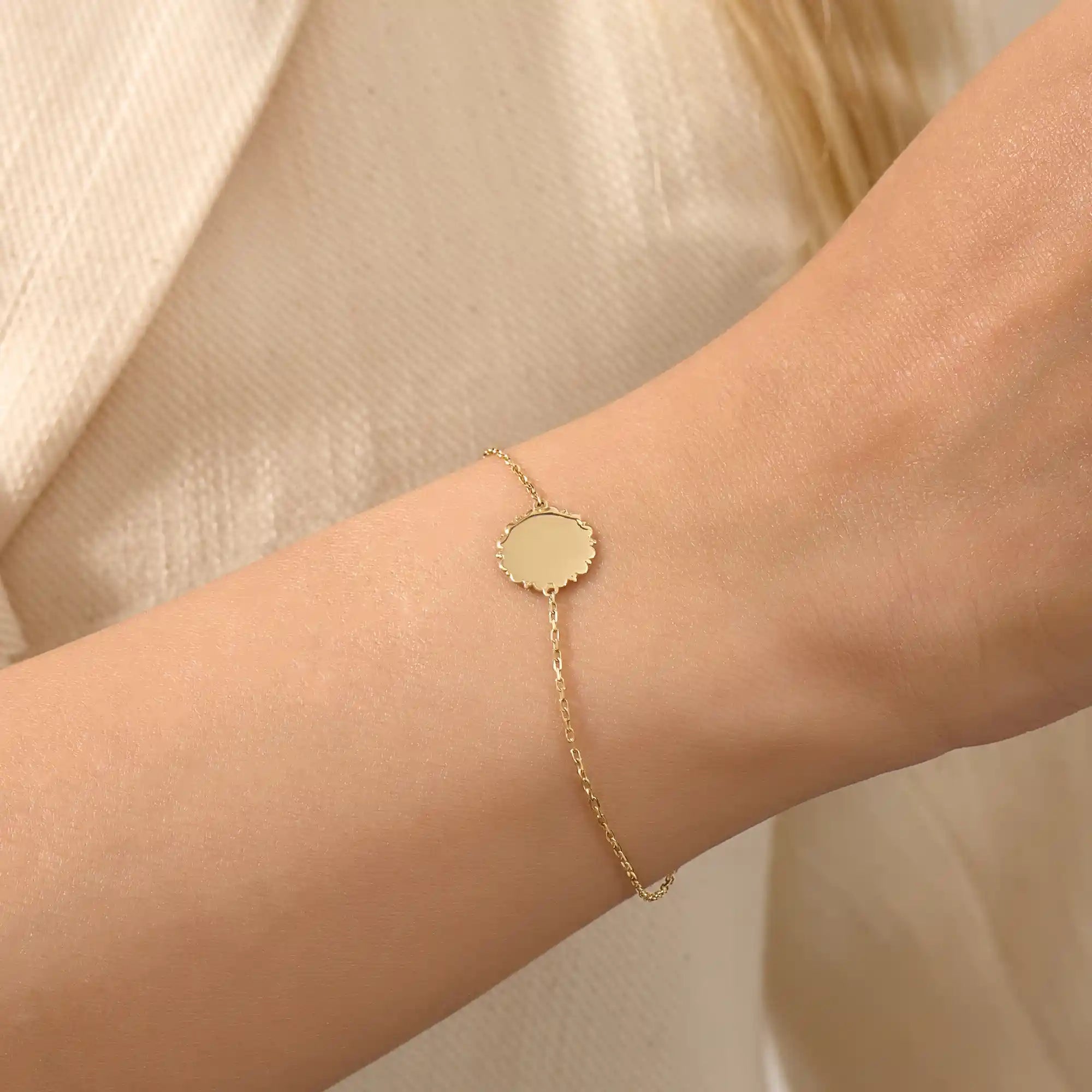 Close-up of a model’s wrist wearing a 14k yellow gold sun bracelet with a round medallion and delicate chain design.