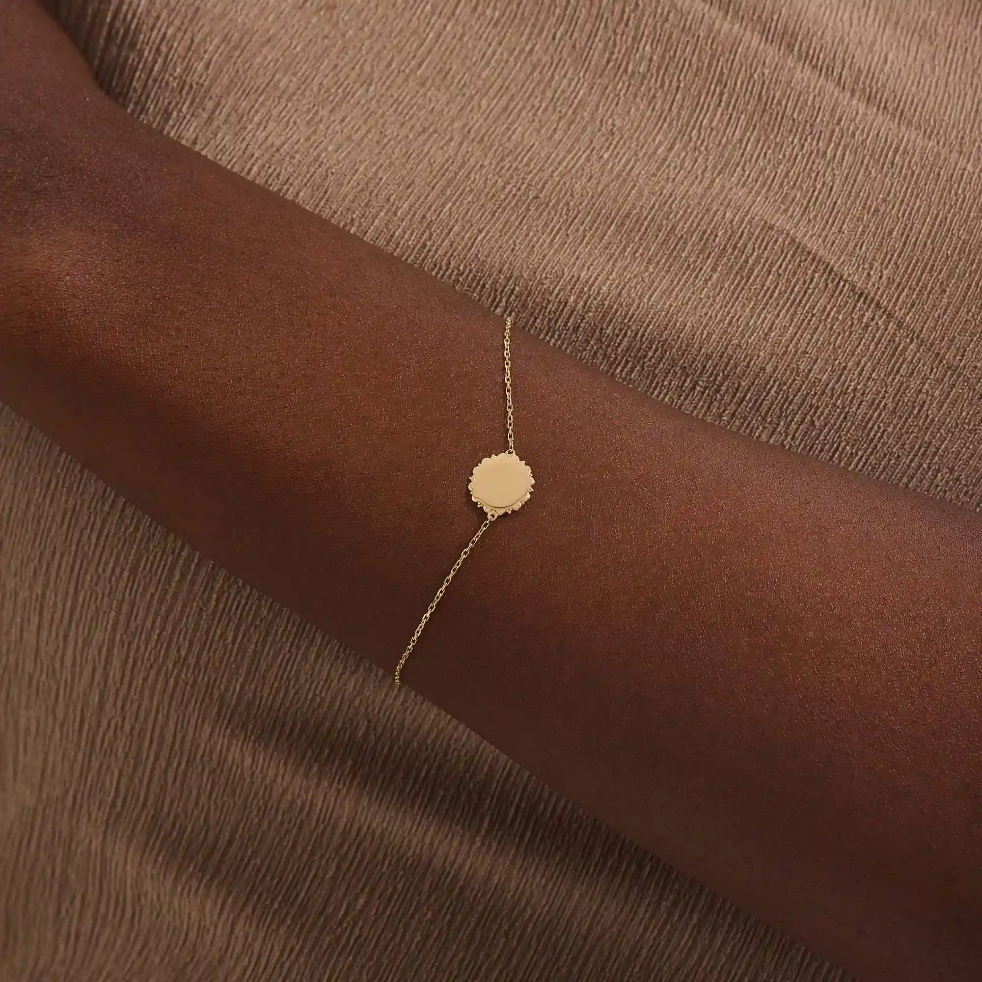 Close-up of a model’s wrist wearing a 14k yellow gold sun bracelet with a round medallion and delicate chain design.