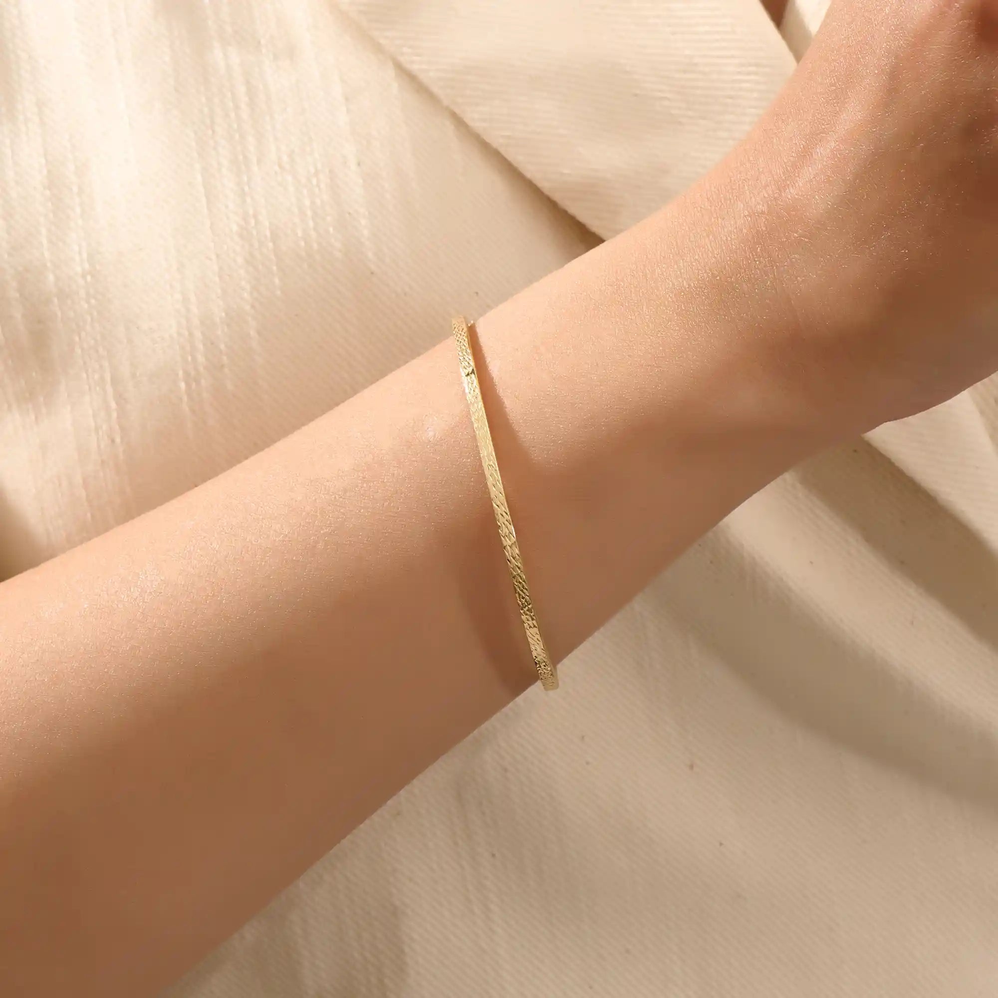 Close-up of a model’s wrist wearing a 14k yellow gold textured square tube bangle with a slim geometric band and polished finish.