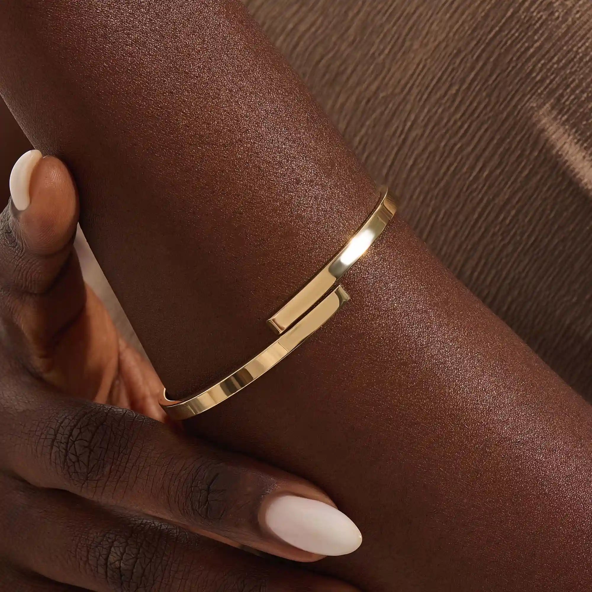 Close-up of a model’s wrist wearing a 14k yellow gold wrap-around bangle with a polished finish and overlapping band detail.