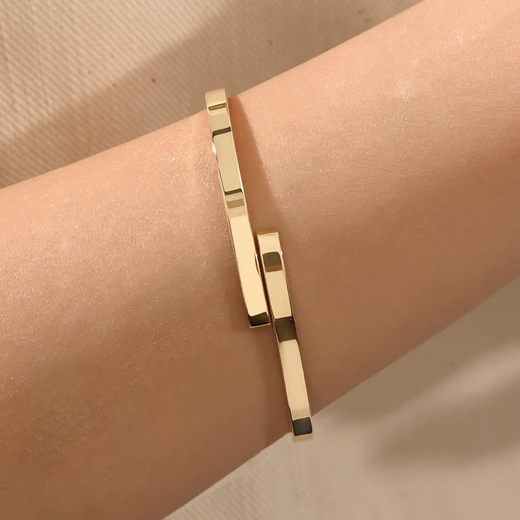 Close-up of a model’s wrist wearing a 14k yellow gold wrap-around bangle with a polished finish and overlapping band detail.
