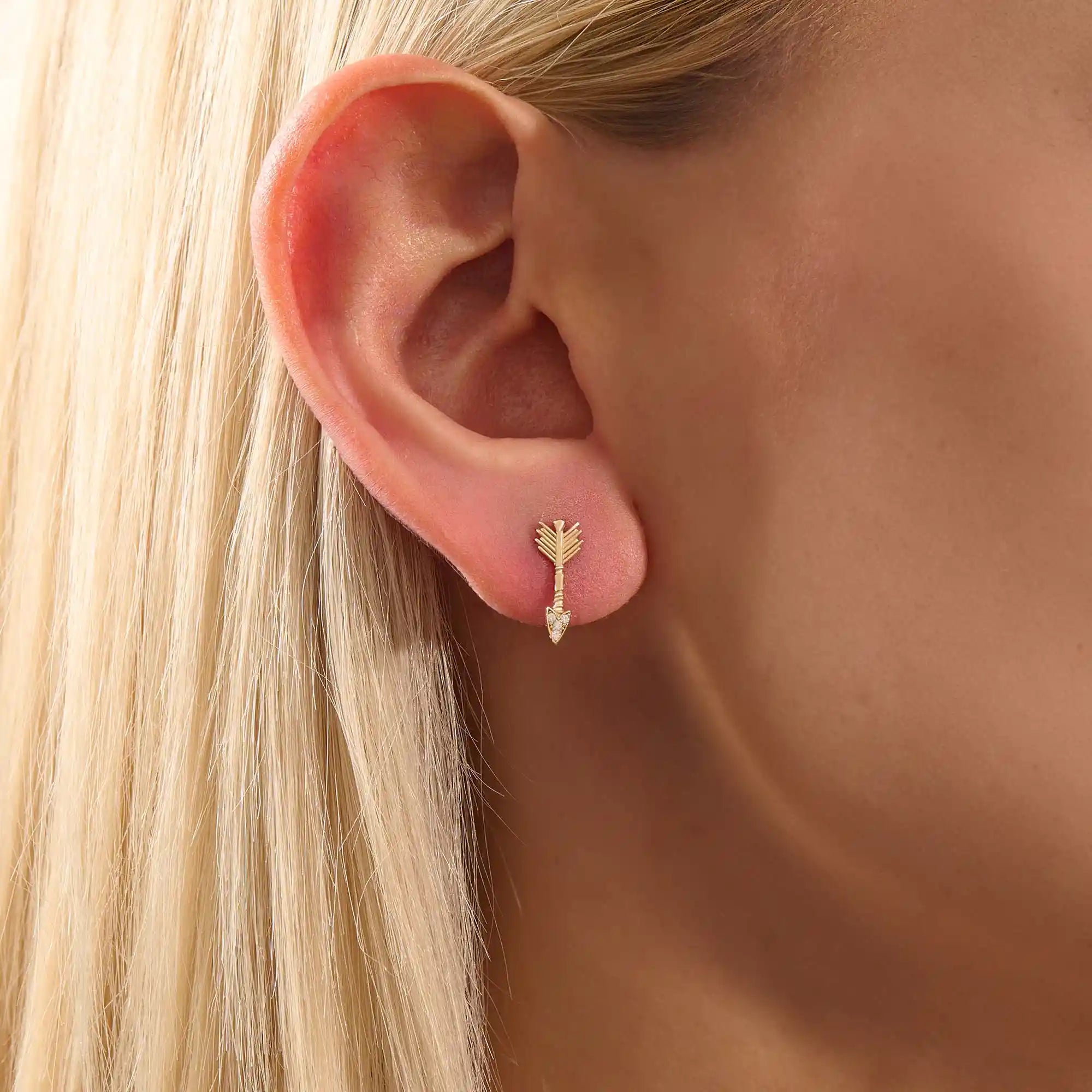 Close-up of a model wearing a 14k solid yellow gold arrow stud earring, showing the sparkle of moissanite stones in the arrowhead.