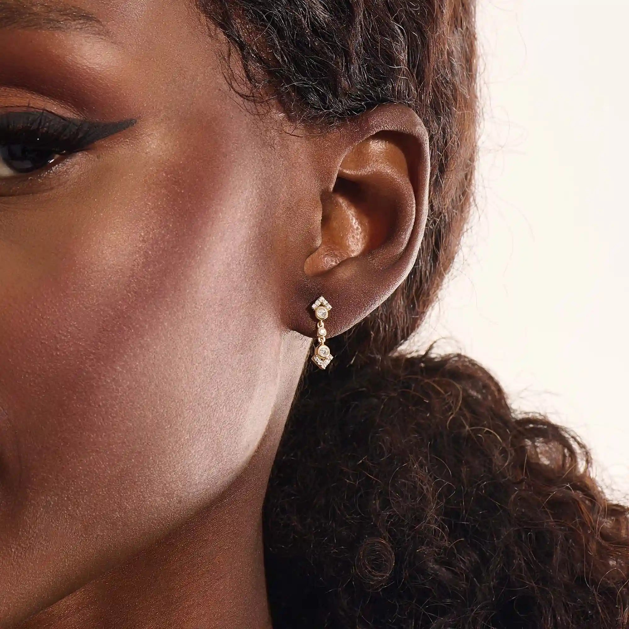 Close-up of a model wearing a 14k solid yellow gold dangling arrow stud earring with sparkling moissanites in bezel and pavé settings.