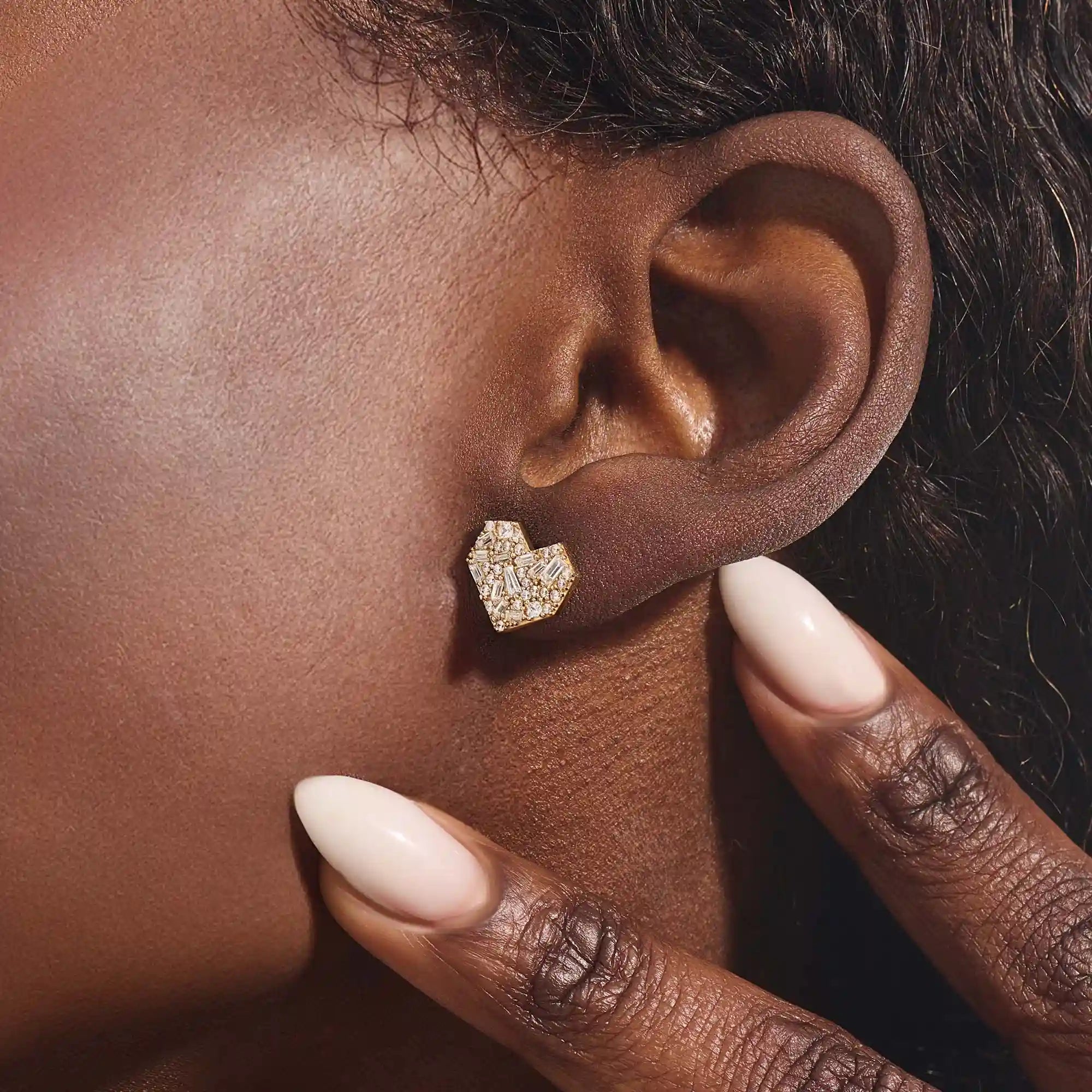 Close-up of a model wearing a 14k solid yellow gold mixed-cut heart stud earring, showcasing the sparkle of baguette and round white moissanite stones.