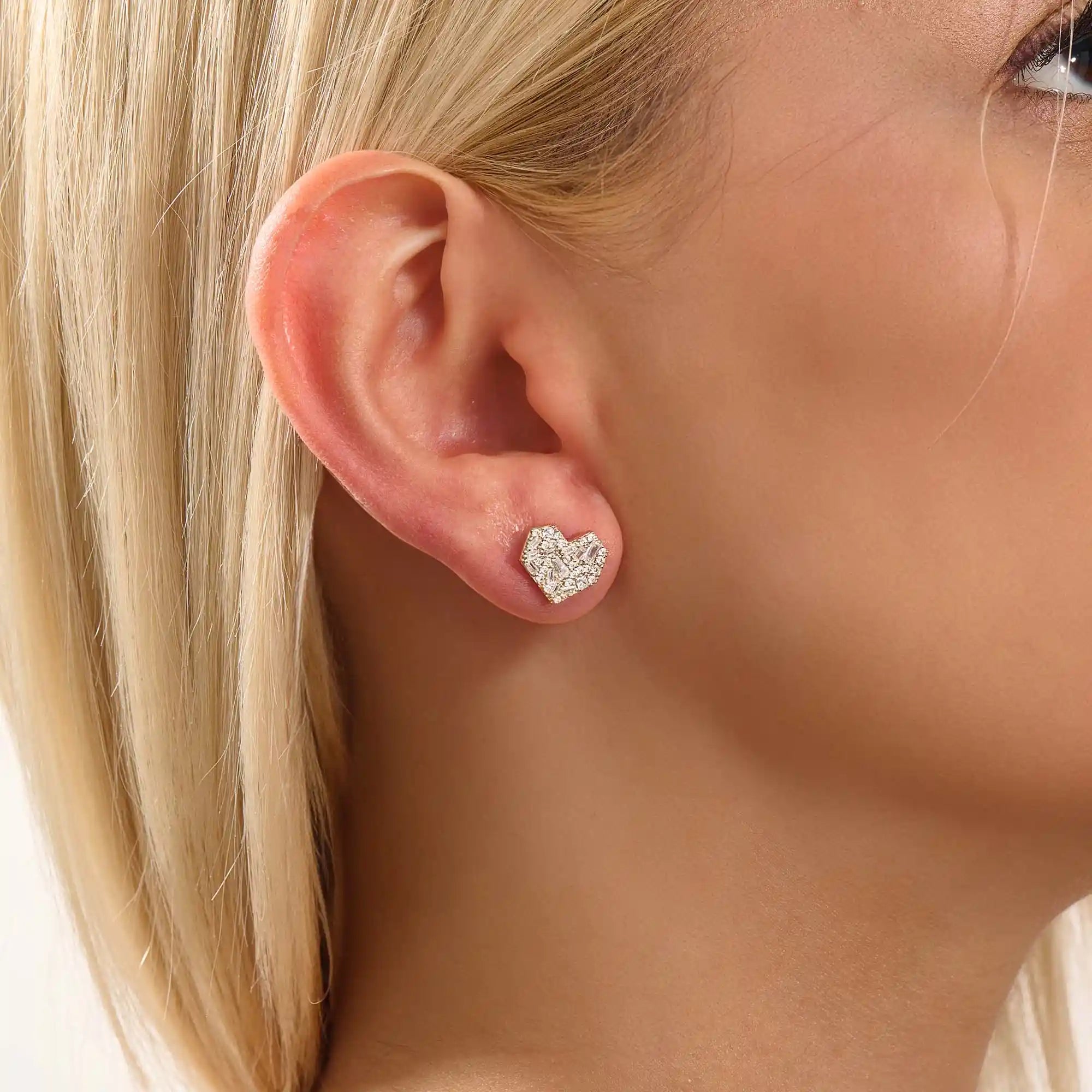Close-up of a model wearing a 14k solid yellow gold mixed-cut heart stud earring, showcasing the sparkle of baguette and round white moissanite stones.