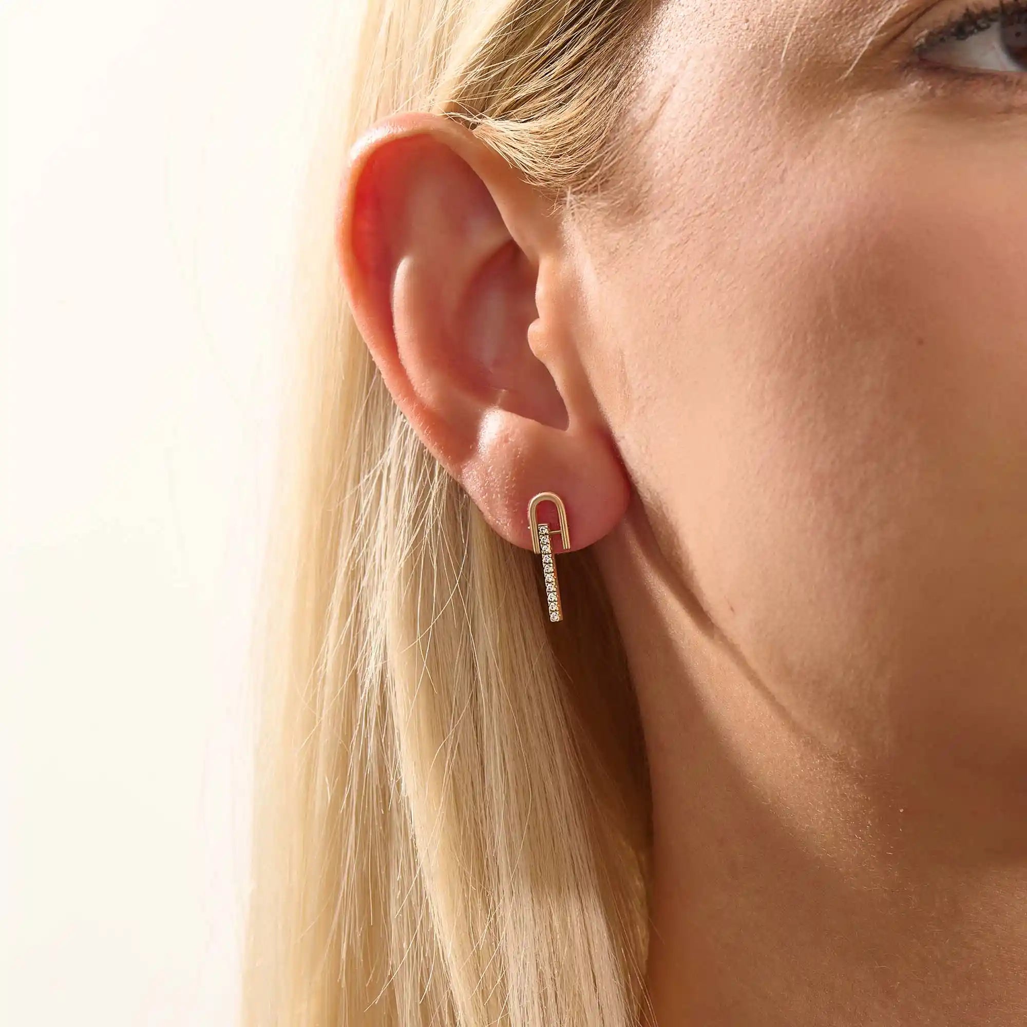 Close-up of a model wearing a 14k yellow gold U-top bar stud earring with a line of brilliant moissanite stones.