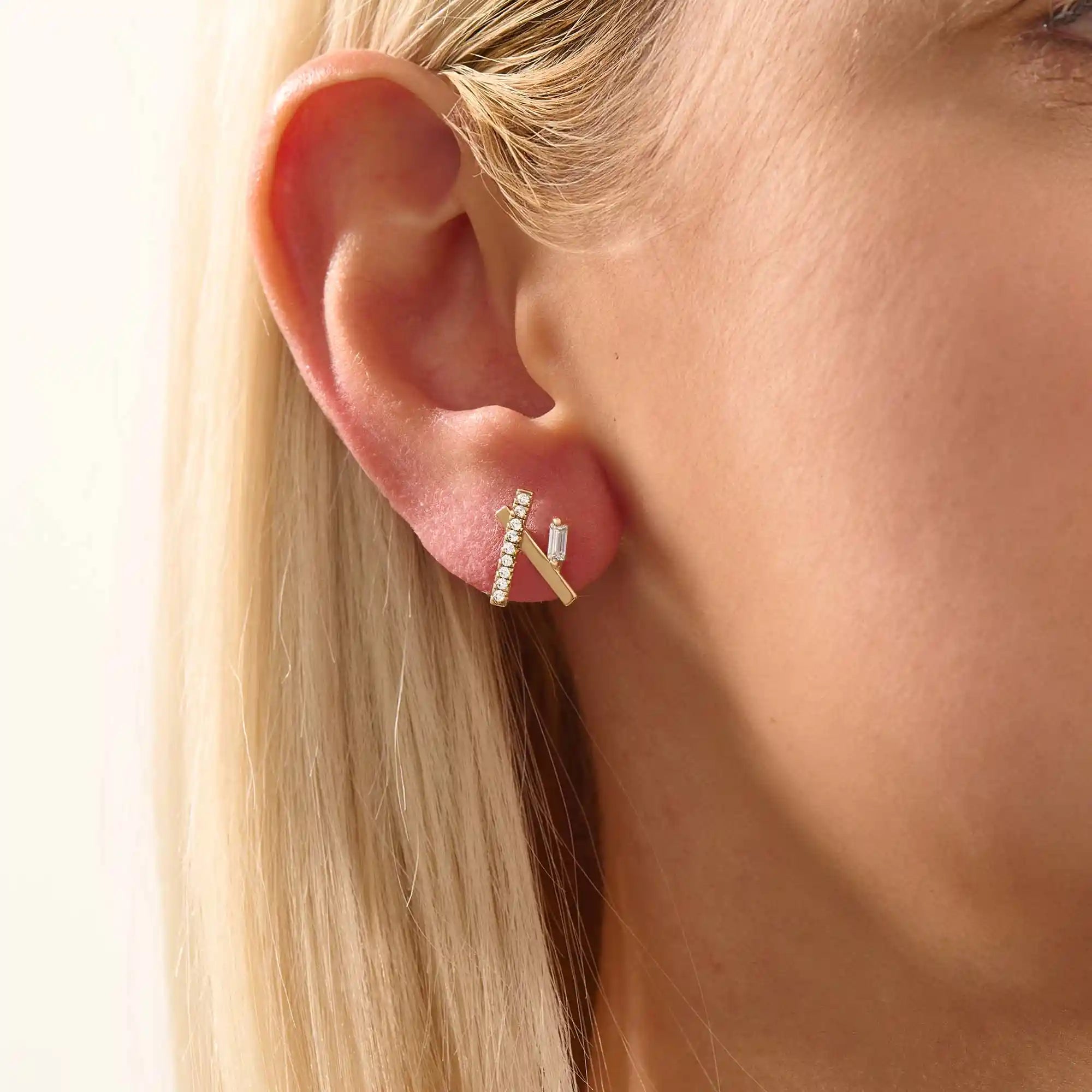 Close-up of a model wearing a 14k yellow gold bar stud with moissanite row and baguette-cut accent stone.