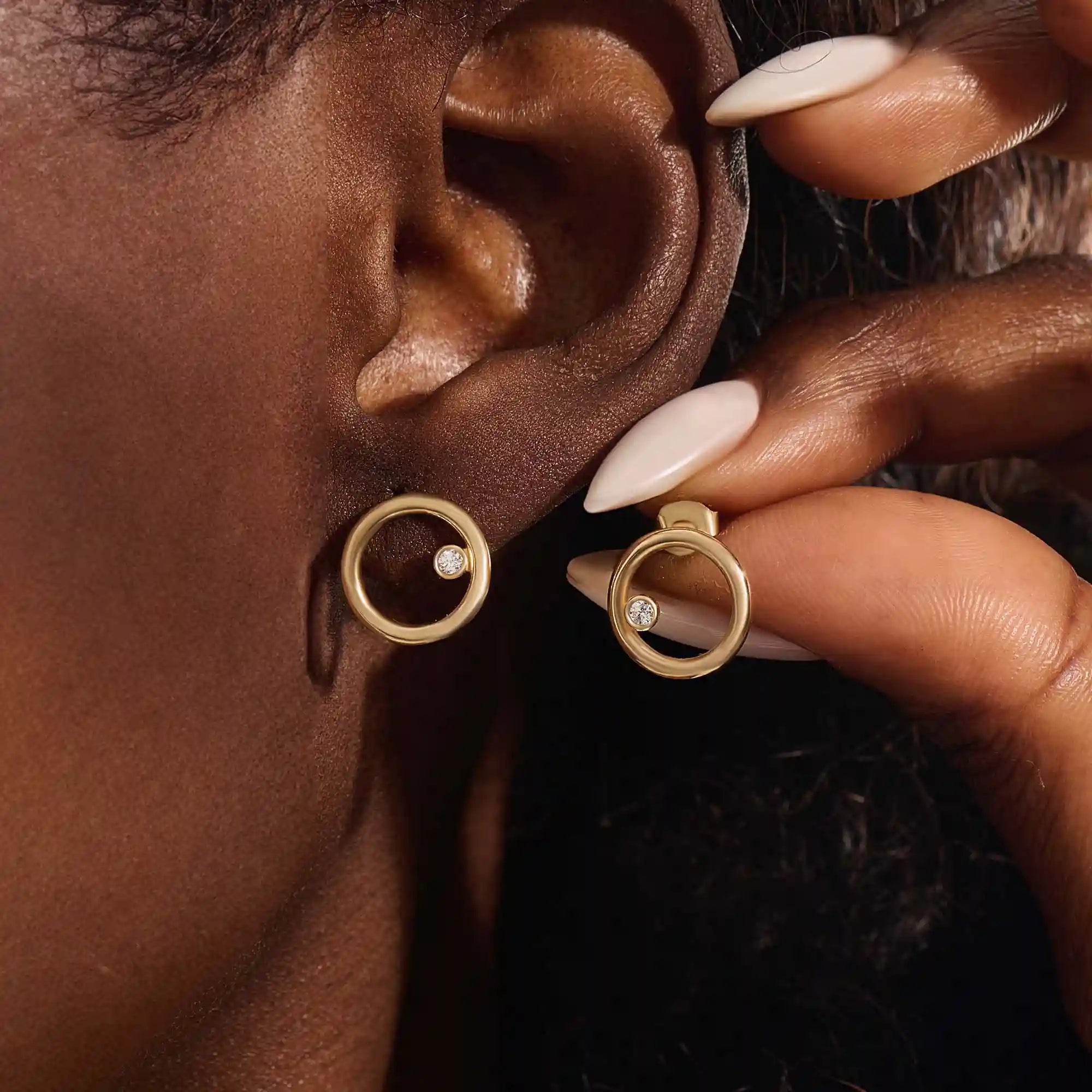 Close-up of a model wearing a 14k yellow gold karma circle stud with a single bezel-set moissanite detail.