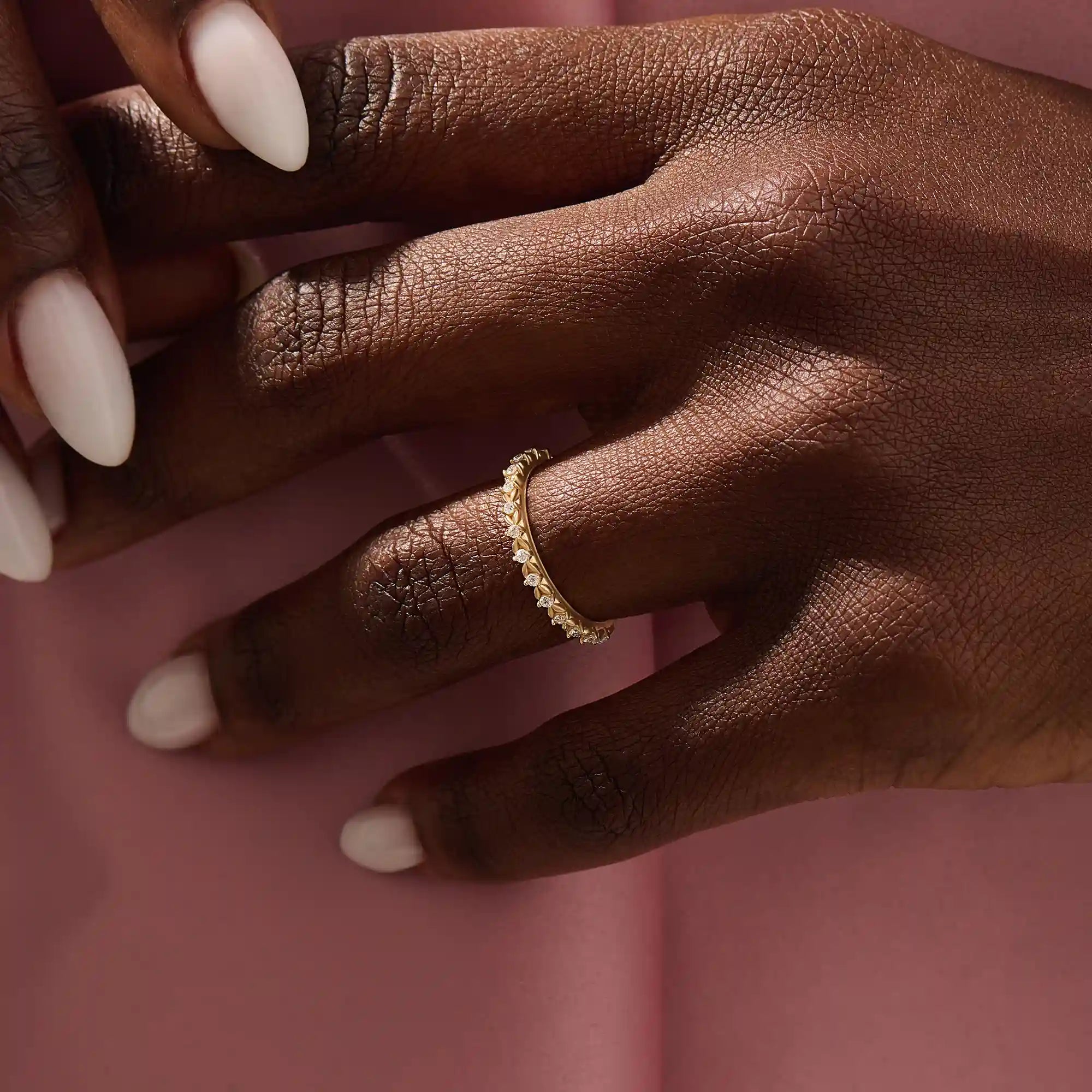 Close-up of a woman’s hand wearing a 14k solid yellow gold eternity band with round brilliant cut moissanite stones in leaf motif prong settings, minimal and elegant bridal jewelry
