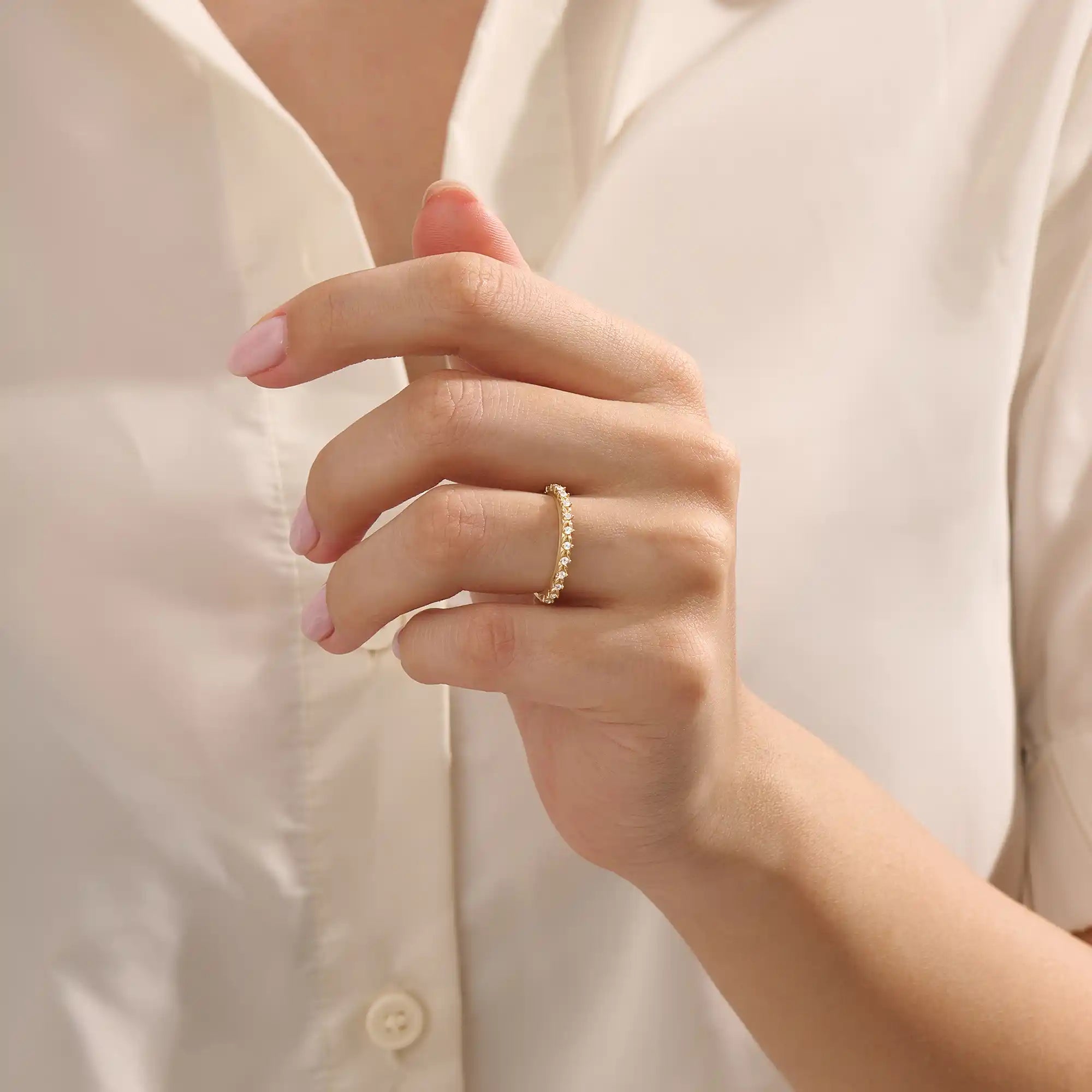 Close-up of a woman’s hand wearing a 14k solid yellow gold eternity band with round brilliant cut moissanite stones in leaf motif prong settings, minimal and elegant bridal jewelry