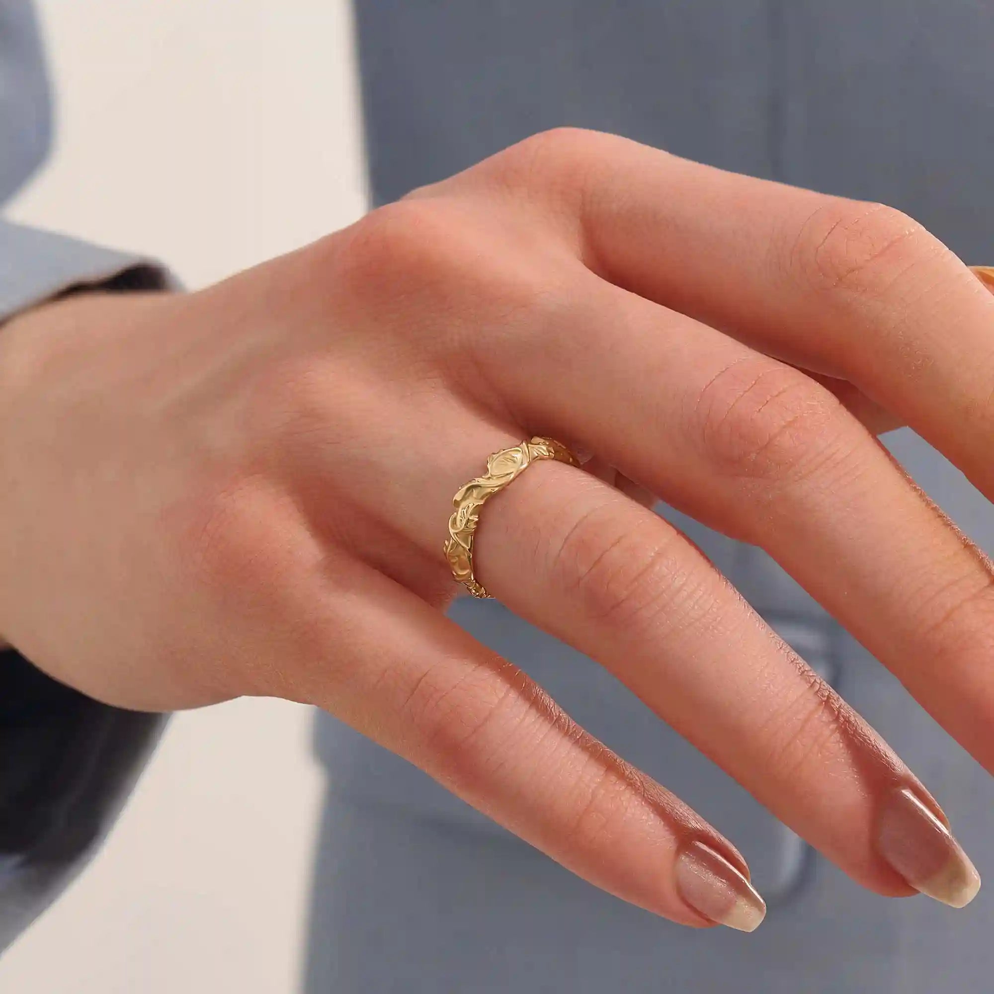 Close-up of a woman's hand wearing a 14k solid yellow gold ivy leaf wedding band. The detailed leaf motifs and smooth polished interior reflect a blend of natural inspiration and artisan craftsmanship, making it a distinctive and elegant choice for daily wear or special occasions.