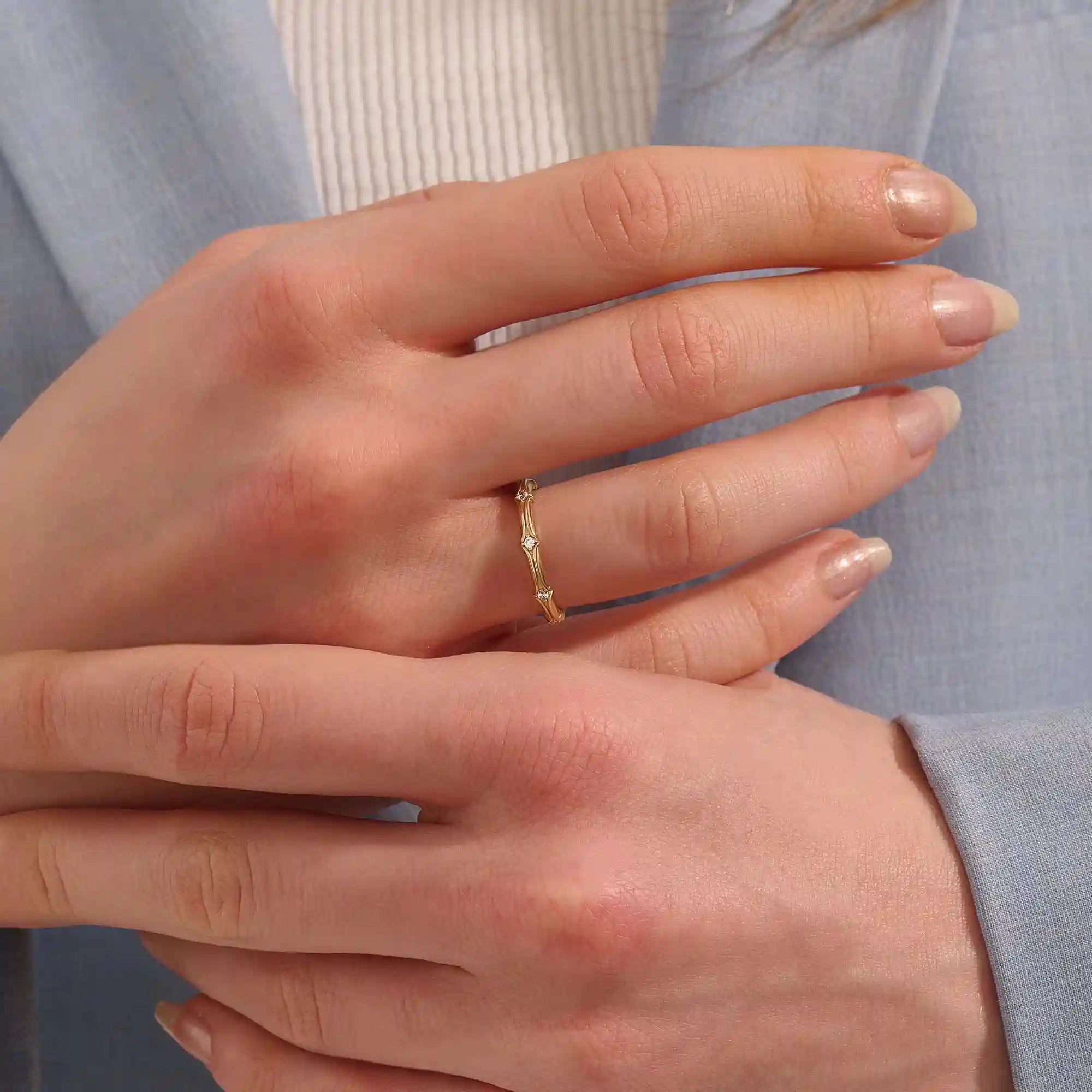 Close-up of a woman wearing a 14k solid yellow gold bamboo-inspired wedding band with evenly spaced moissanites
