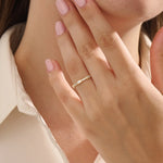 Close-up of a woman wearing a 14k solid yellow gold band with a baguette cut moissanite center stone and round brilliant cut moissanite accents, minimal and modern fine jewelry