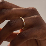 Close-up of a woman wearing a 14k solid yellow gold band with a baguette cut moissanite center stone and round brilliant cut moissanite accents, minimal and modern fine jewelry