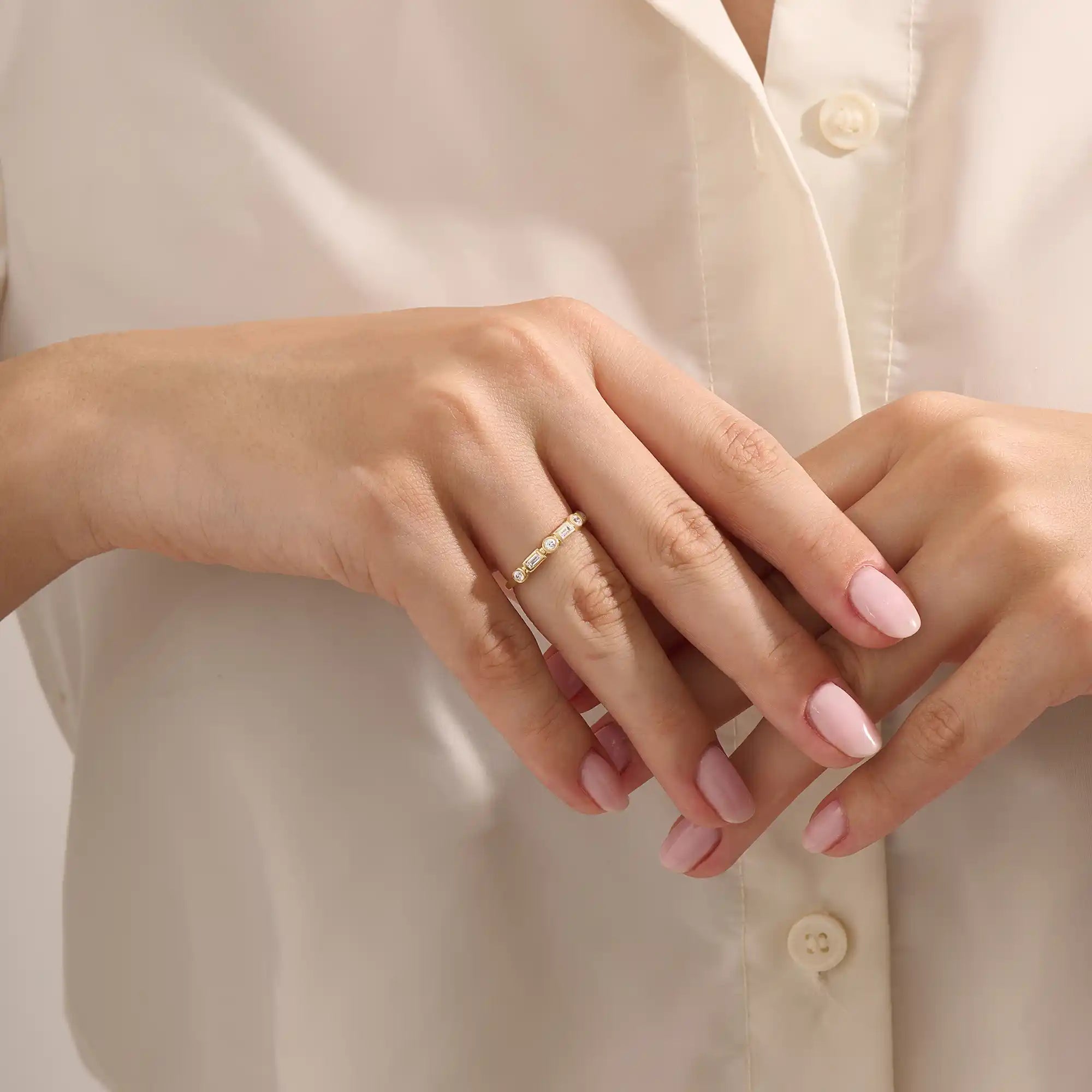 Close-up of a woman wearing a 14k solid yellow gold band with alternating baguette cut and round brilliant cut moissanite stones in a bezel setting, minimal and modern wedding or stacking ring