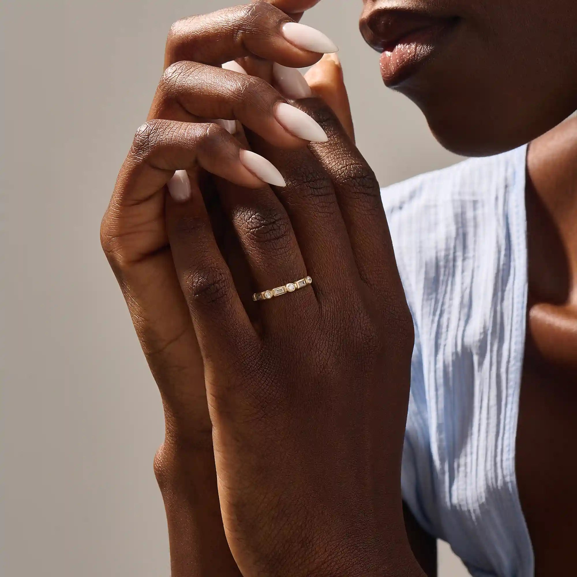 Close-up of a woman wearing a 14k solid yellow gold band with alternating baguette cut and round brilliant cut moissanite stones in a bezel setting, minimal and modern wedding or stacking ring