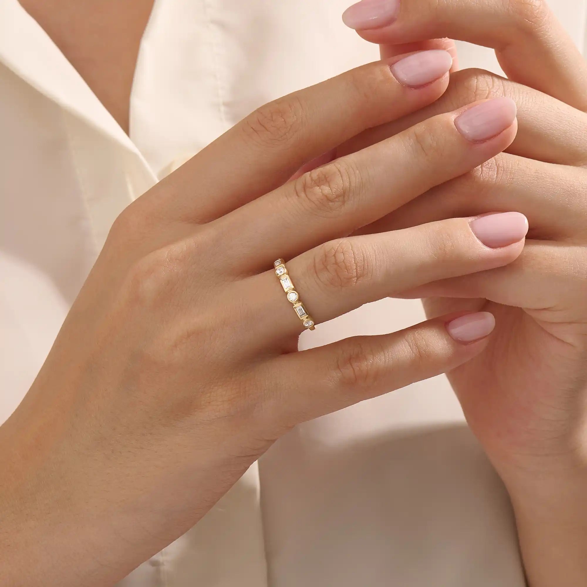 Close-up of a woman wearing a 14k solid yellow gold band with alternating baguette cut and round brilliant cut moissanite stones in a bezel setting, minimal and modern wedding or stacking ring