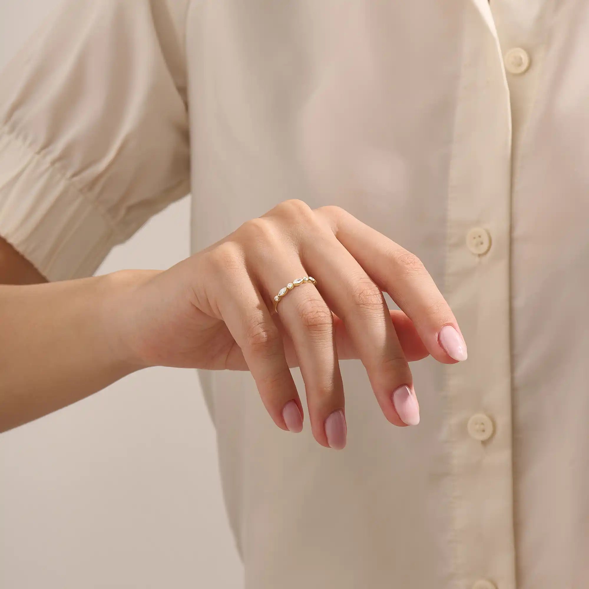 Close-up of a woman wearing a 14k solid yellow gold band with alternating marquise cut and round brilliant cut moissanite stones in a bezel setting, minimal and elegant bridal jewelry