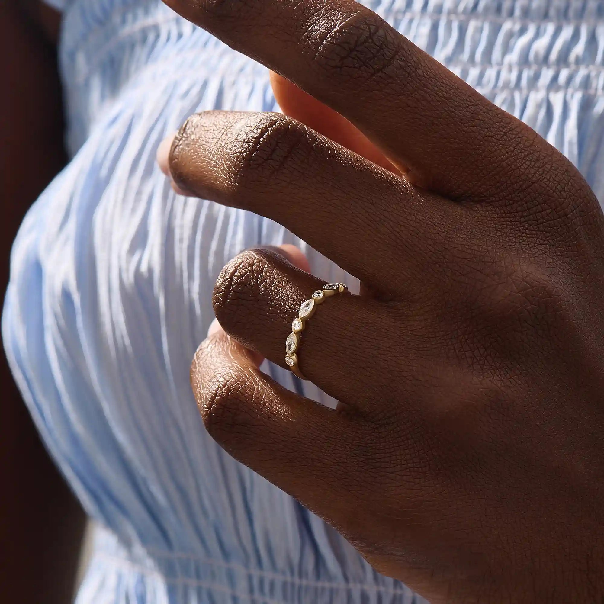 Close-up of a woman wearing a 14k solid yellow gold band with alternating marquise cut and round brilliant cut moissanite stones in a bezel setting, minimal and elegant bridal jewelry