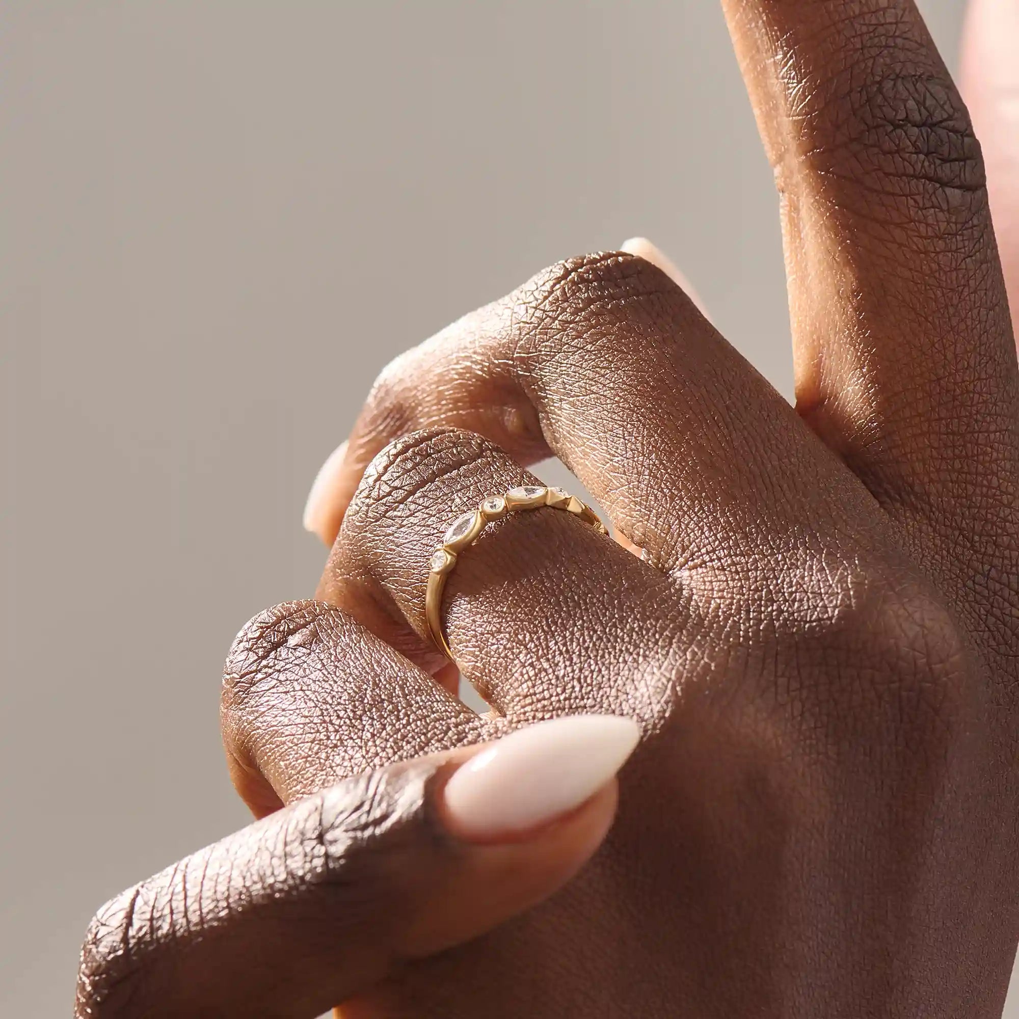 Close-up of a woman wearing a 14k solid yellow gold band with alternating marquise cut and round brilliant cut moissanite stones in a bezel setting, minimal and elegant bridal jewelry
d