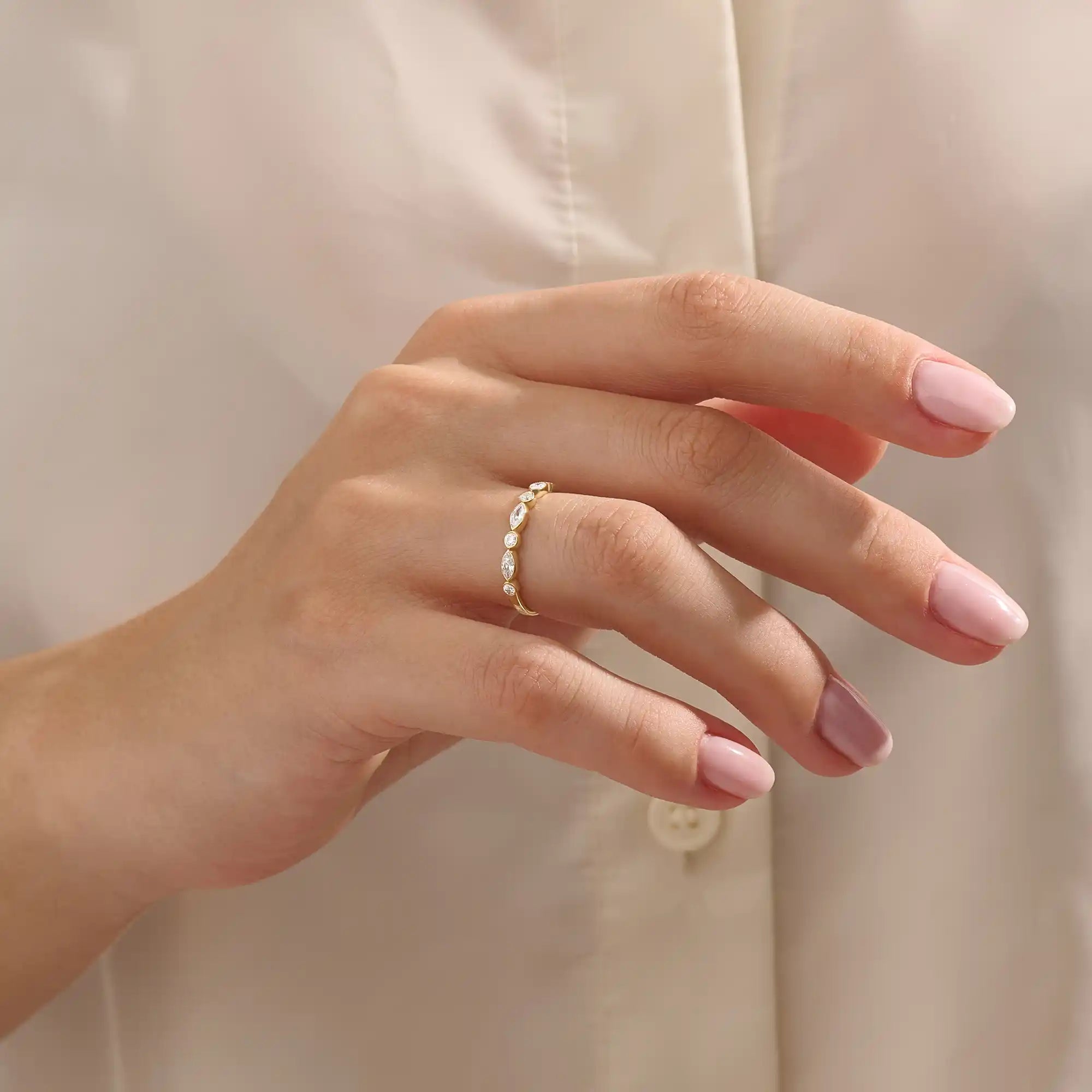 Close-up of a woman wearing a 14k solid yellow gold band with alternating marquise cut and round brilliant cut moissanite stones in a bezel setting, minimal and elegant bridal jewelry