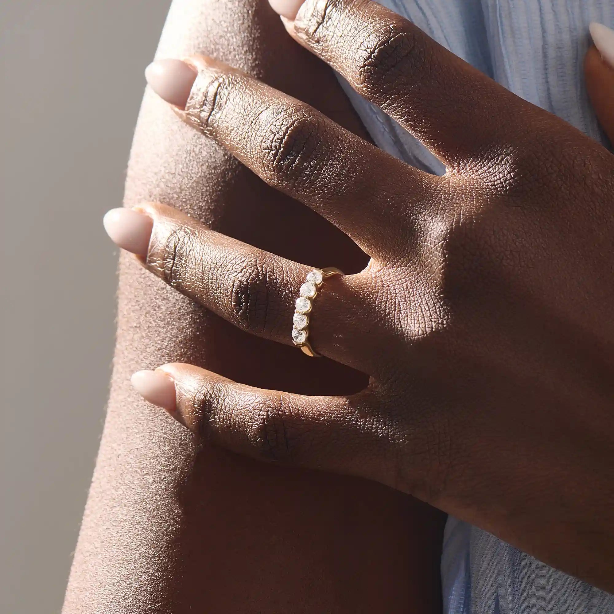 Close-up of a woman wearing a 14k solid yellow gold band with five round brilliant cut moissanite stones in a prong setting and engraved shank detail, sophisticated wedding or anniversary ring