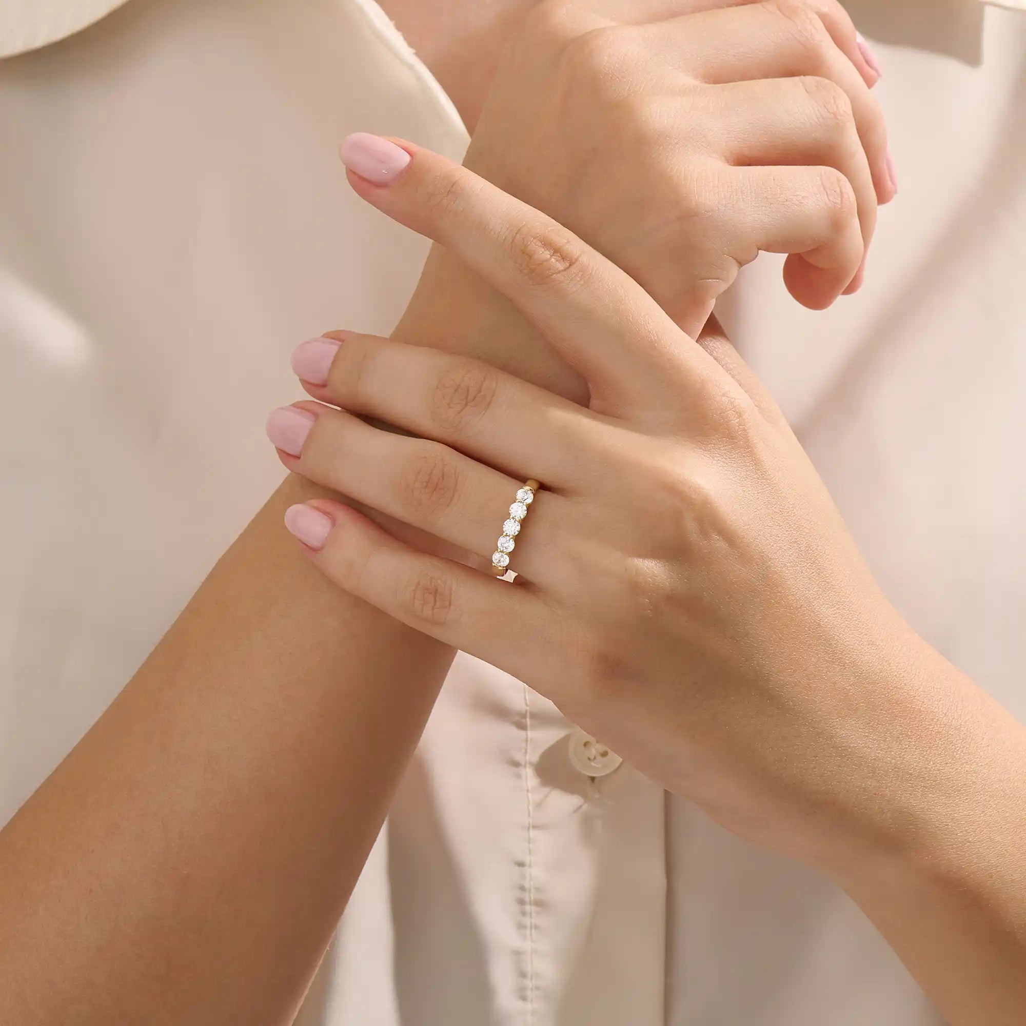 Close-up of a woman wearing a 14k solid yellow gold band with five round brilliant cut moissanite stones in a prong setting and engraved shank detail, sophisticated wedding or anniversary ring
