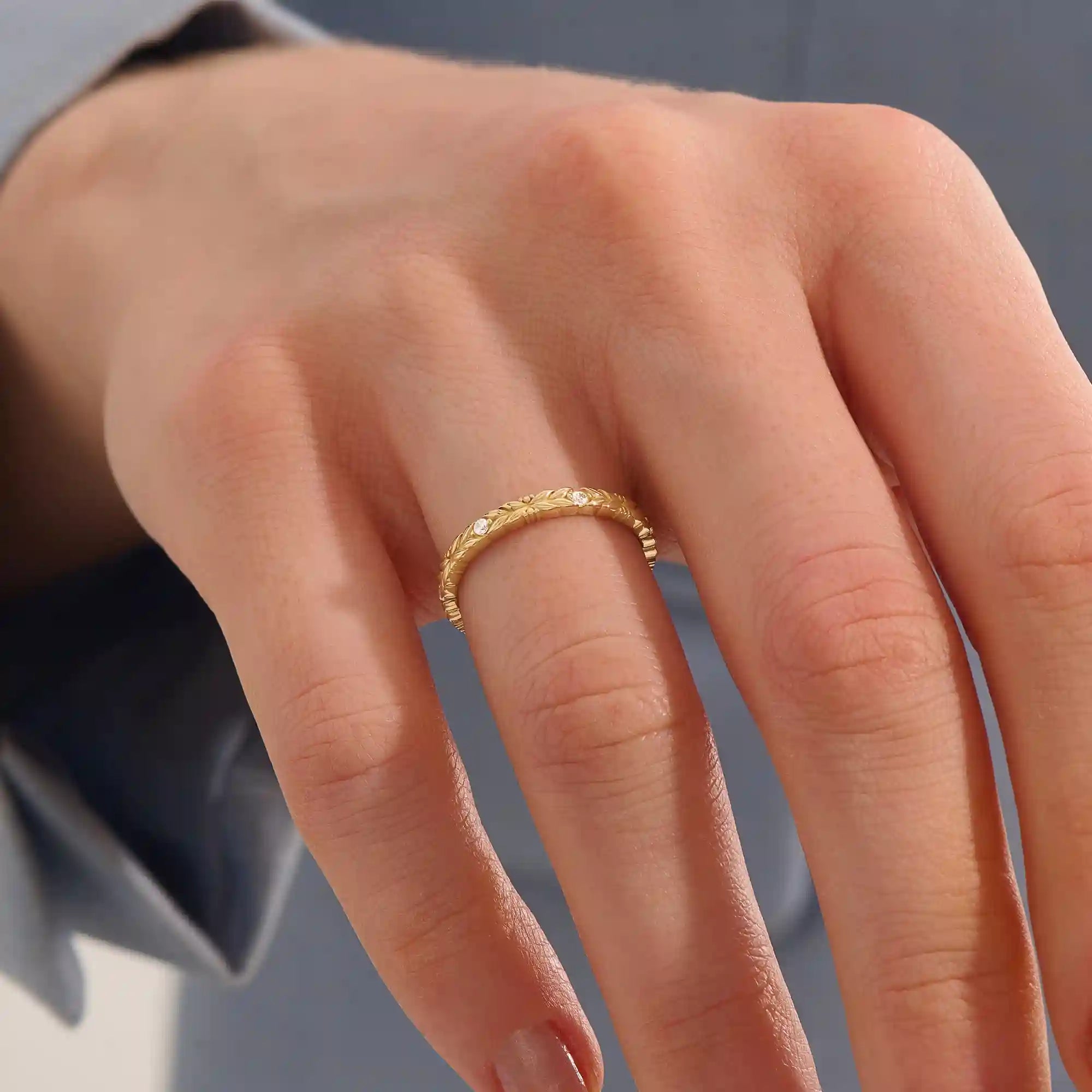 Close-up of a woman wearing a 14k solid yellow gold band with laurel leaf design and bezel set round brilliant cut moissanite stones, elegant and nature-inspired wedding ring