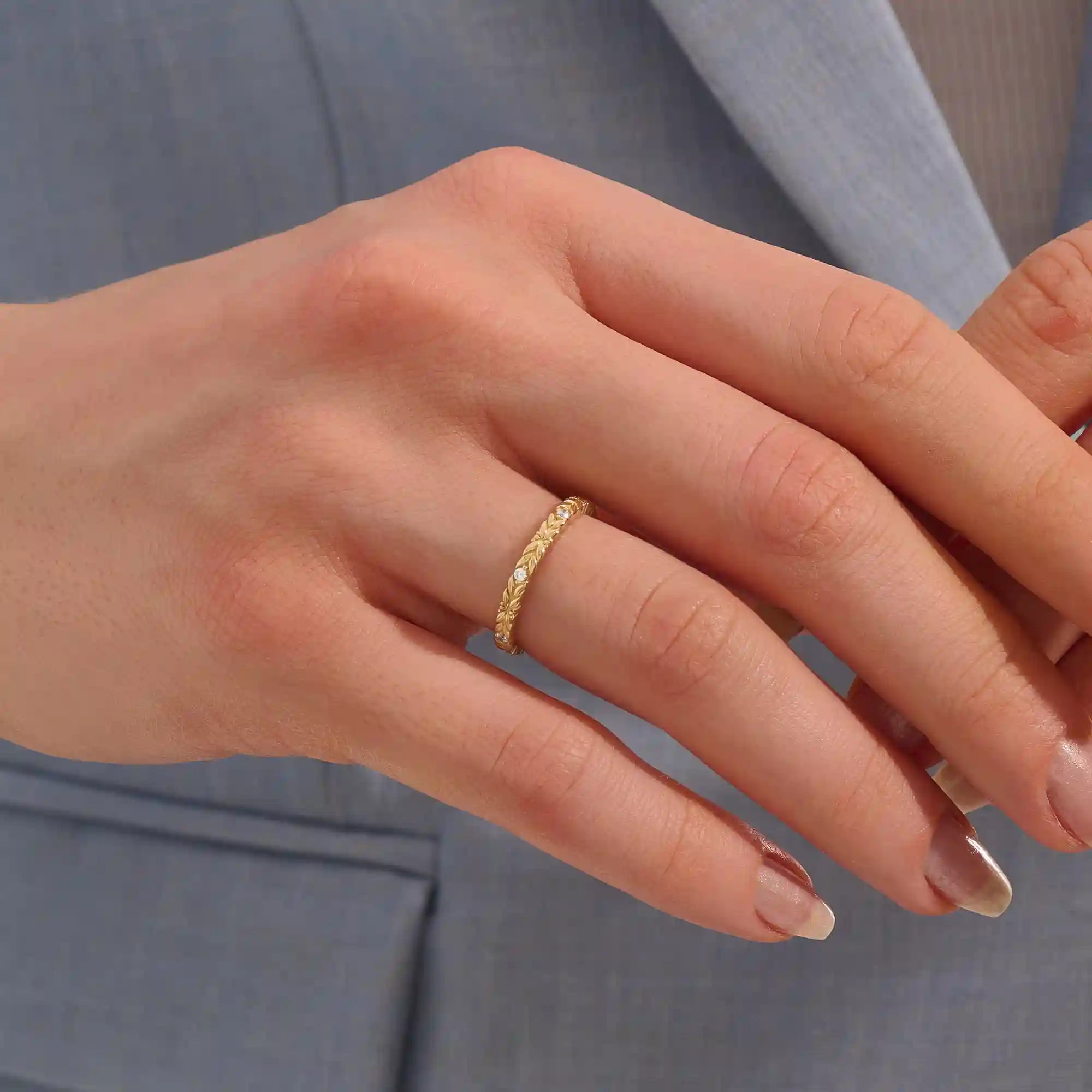Close-up of a woman wearing a 14k solid yellow gold band with laurel leaf design and bezel set round brilliant cut moissanite stones, elegant and nature-inspired wedding ring